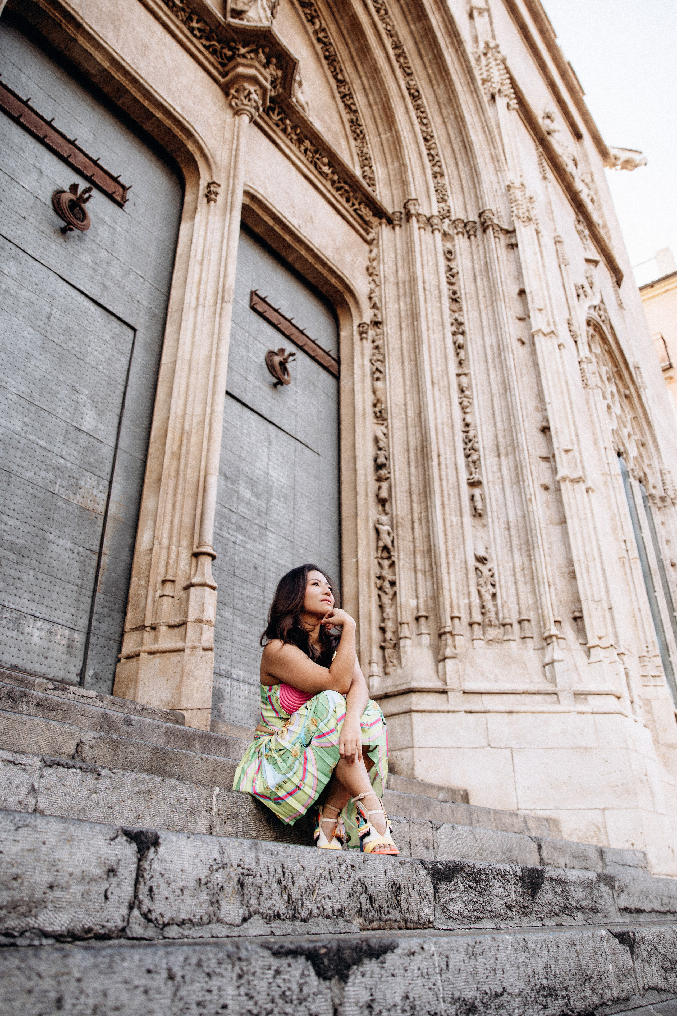Sesión de retrato femenino en Valencia, España, con una mujer sentada en históricos escalones de piedra junto a un elegante edificio mediterráneo. Capturada con suave luz natural para destacar la arquitectura atemporal, la elegancia de la pose y las emociones auténticas, ideal para fotografía de retrato femenino, sesiones individuales, marca personal y retratos lifestyle en Valencia y toda España.