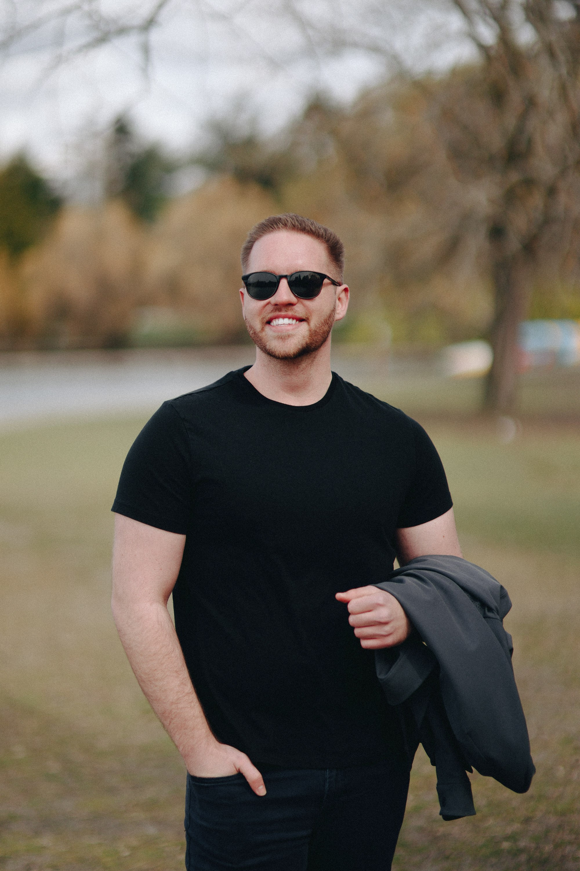Man in black t-shirt and sunglasses, smiling outdoors