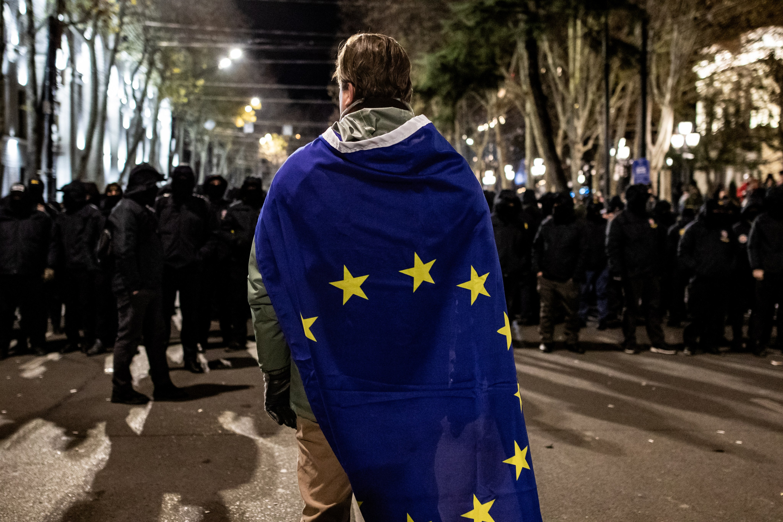 Un manifestant portant un drapeau européen fait face aux forces spéciales.