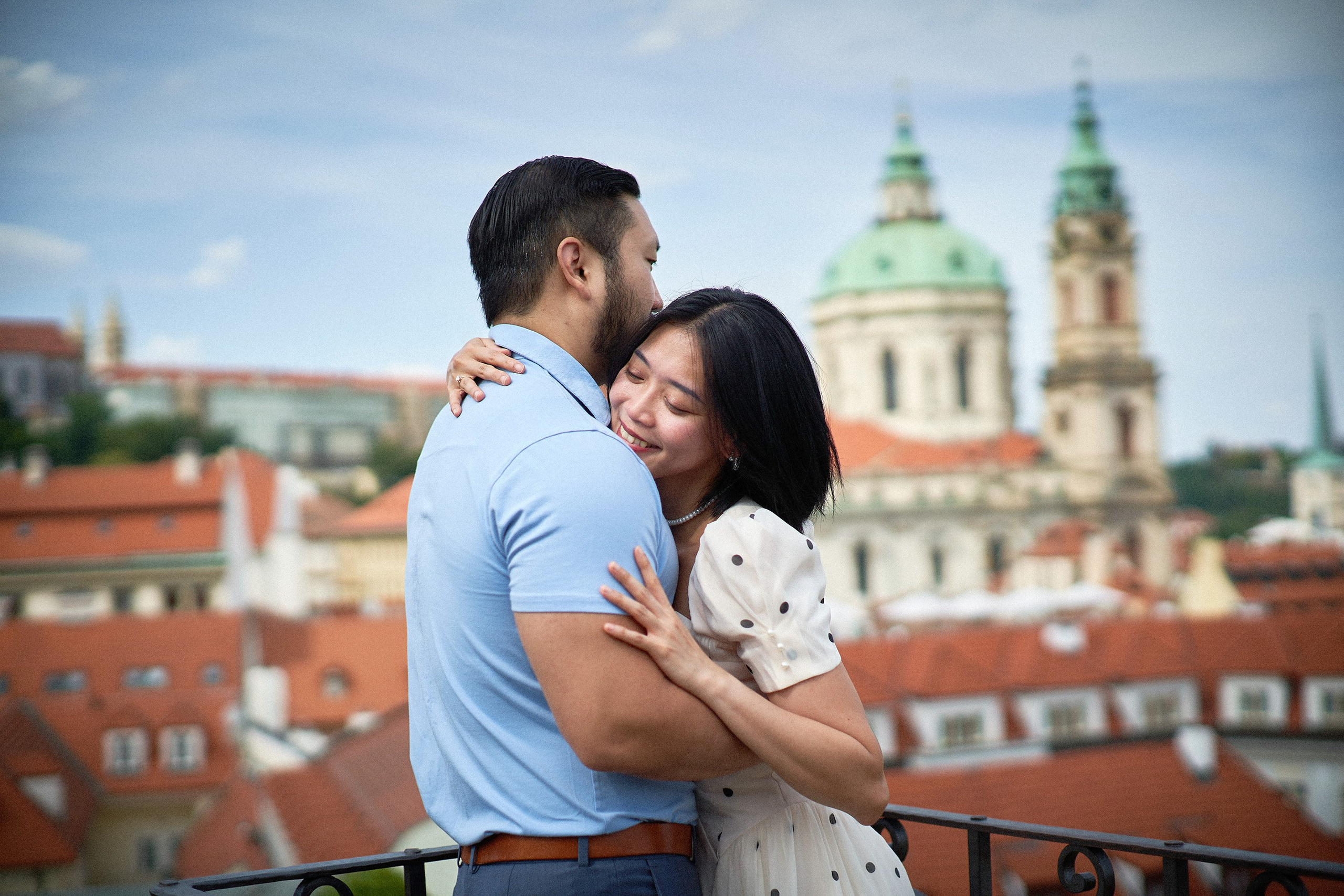 Woman embracing her partner with St. Nicholas Church dome visible in the background, Vrtba Garden.