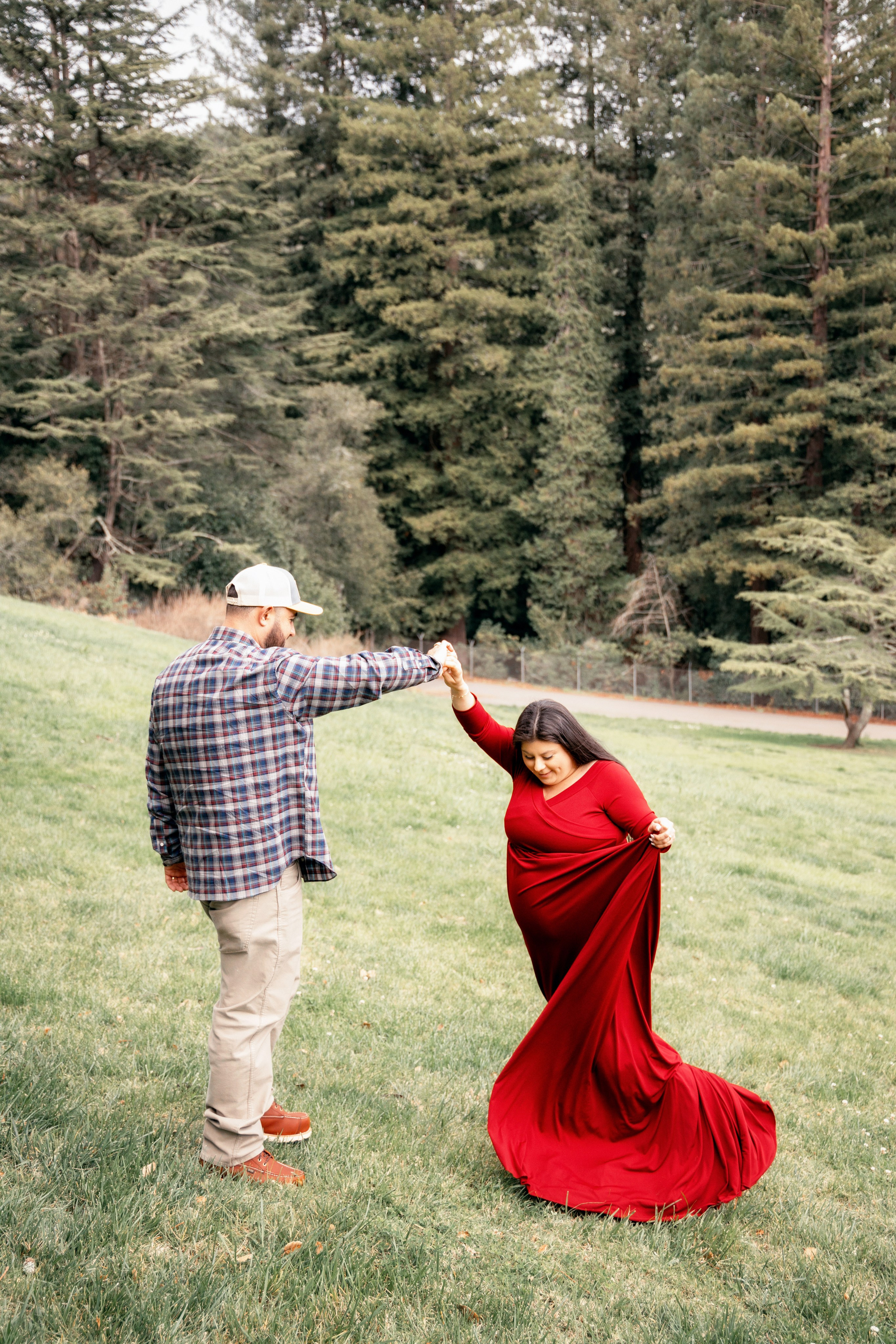 Pregnant woman in a flowing dress among tall trees in the park