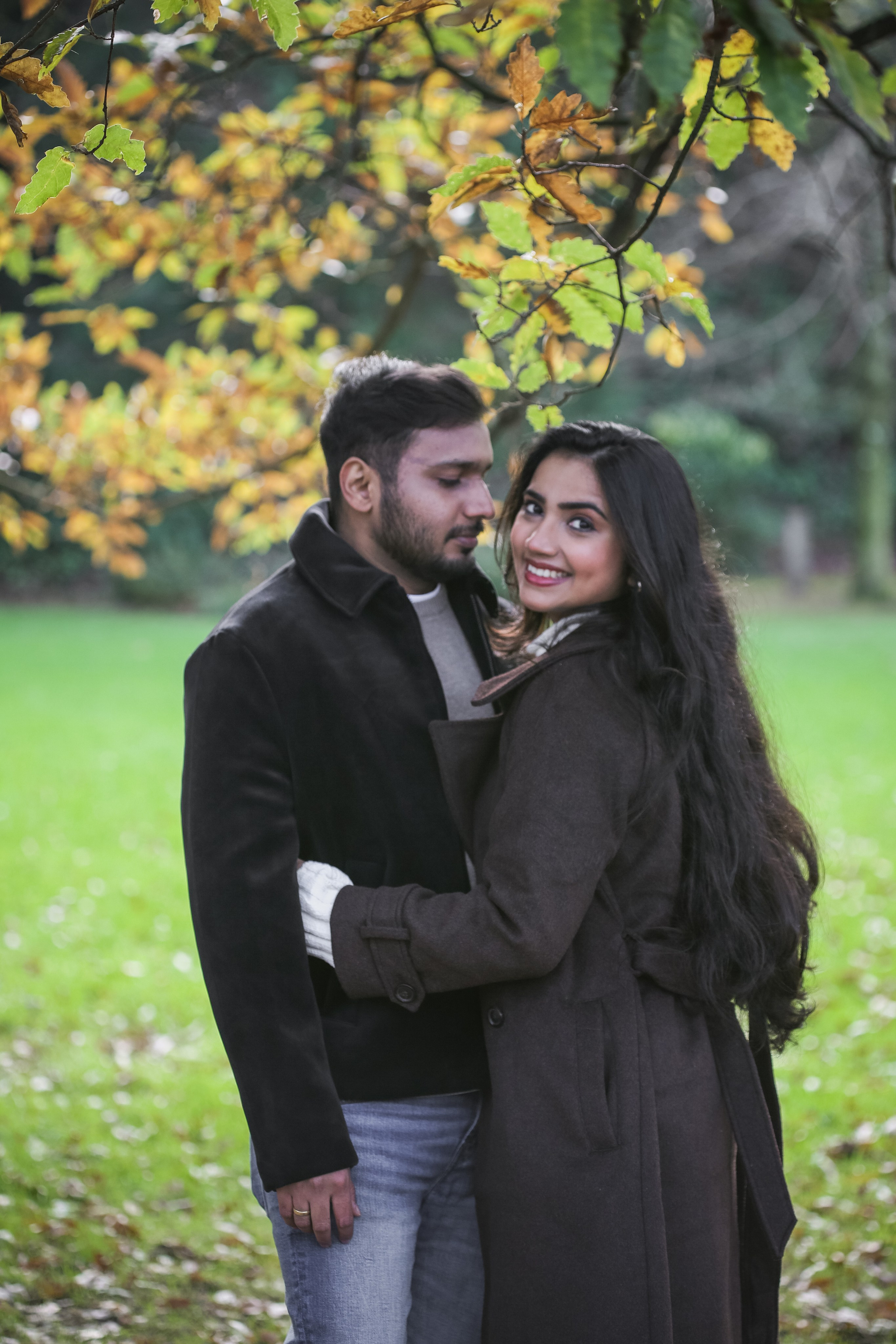 A warm and intimate portrait beneath autumn leaves, capturing closeness, comfort, and a natural sense of ease between two people.