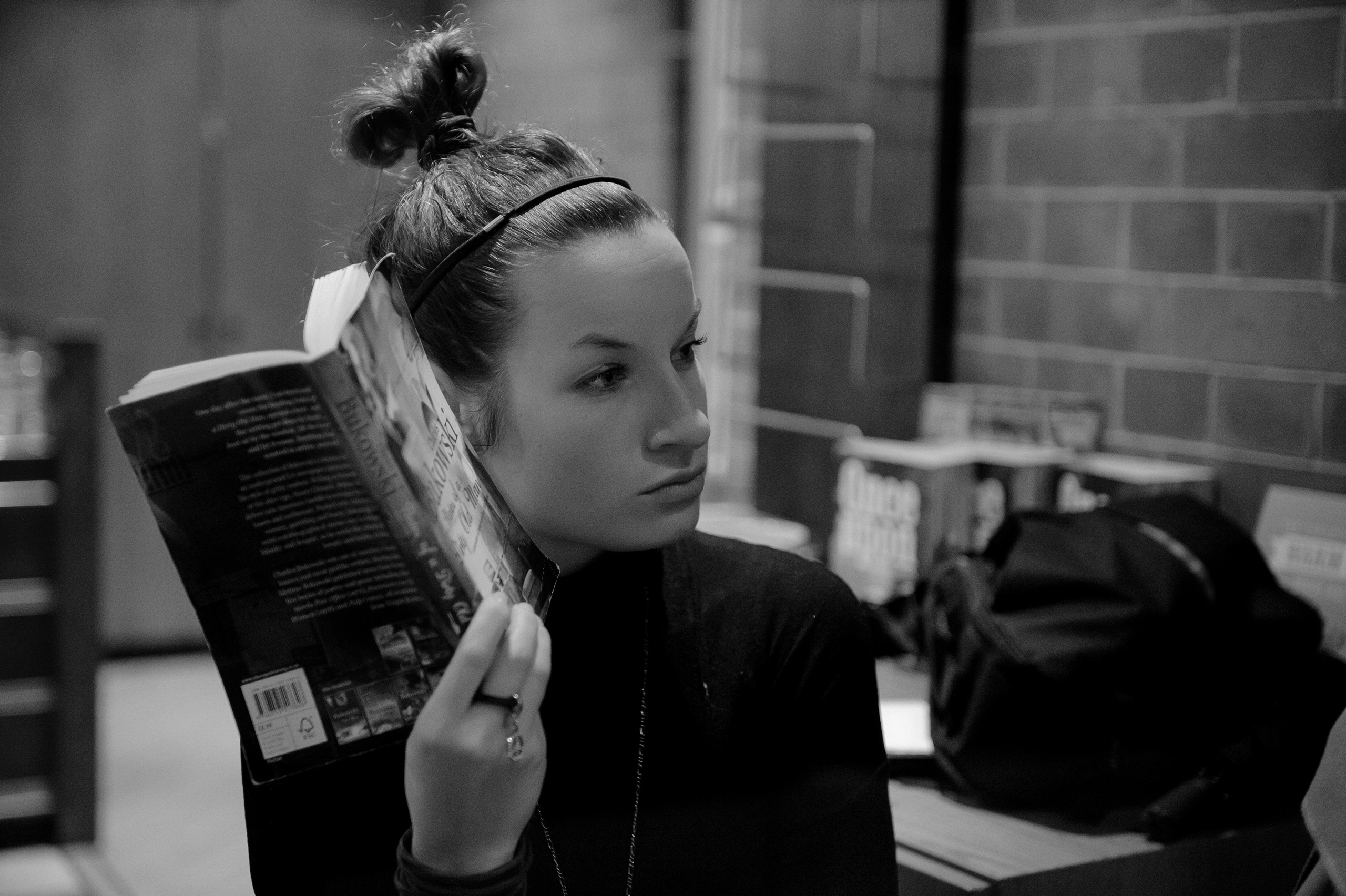 A black and white portrait of a woman holding a book. The woman is sitting in a cafe.