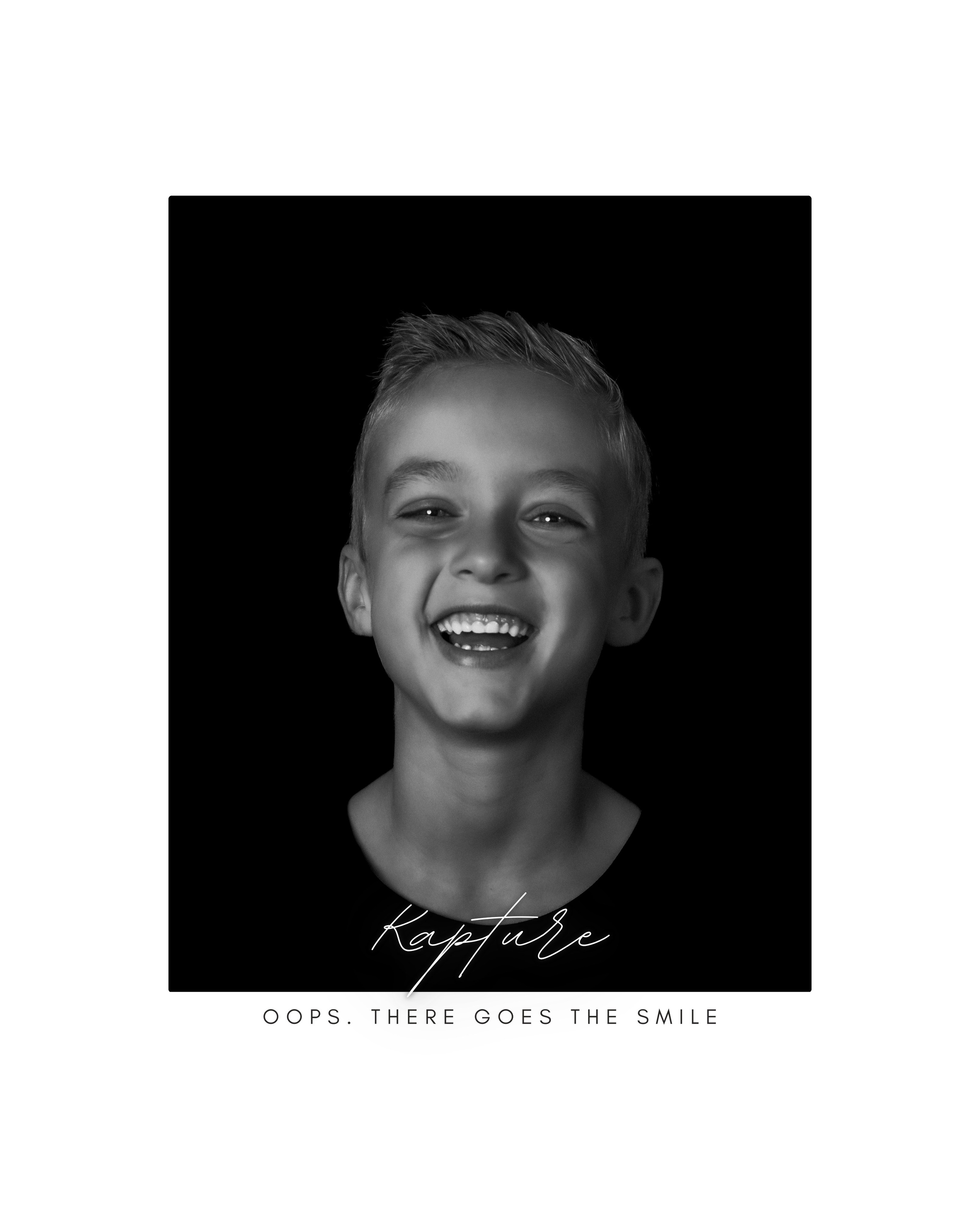 Kapture Fotografie - Zwart-wit portret van een jongen die in de camera kijkt met een speelse, ondeugende glimlach.