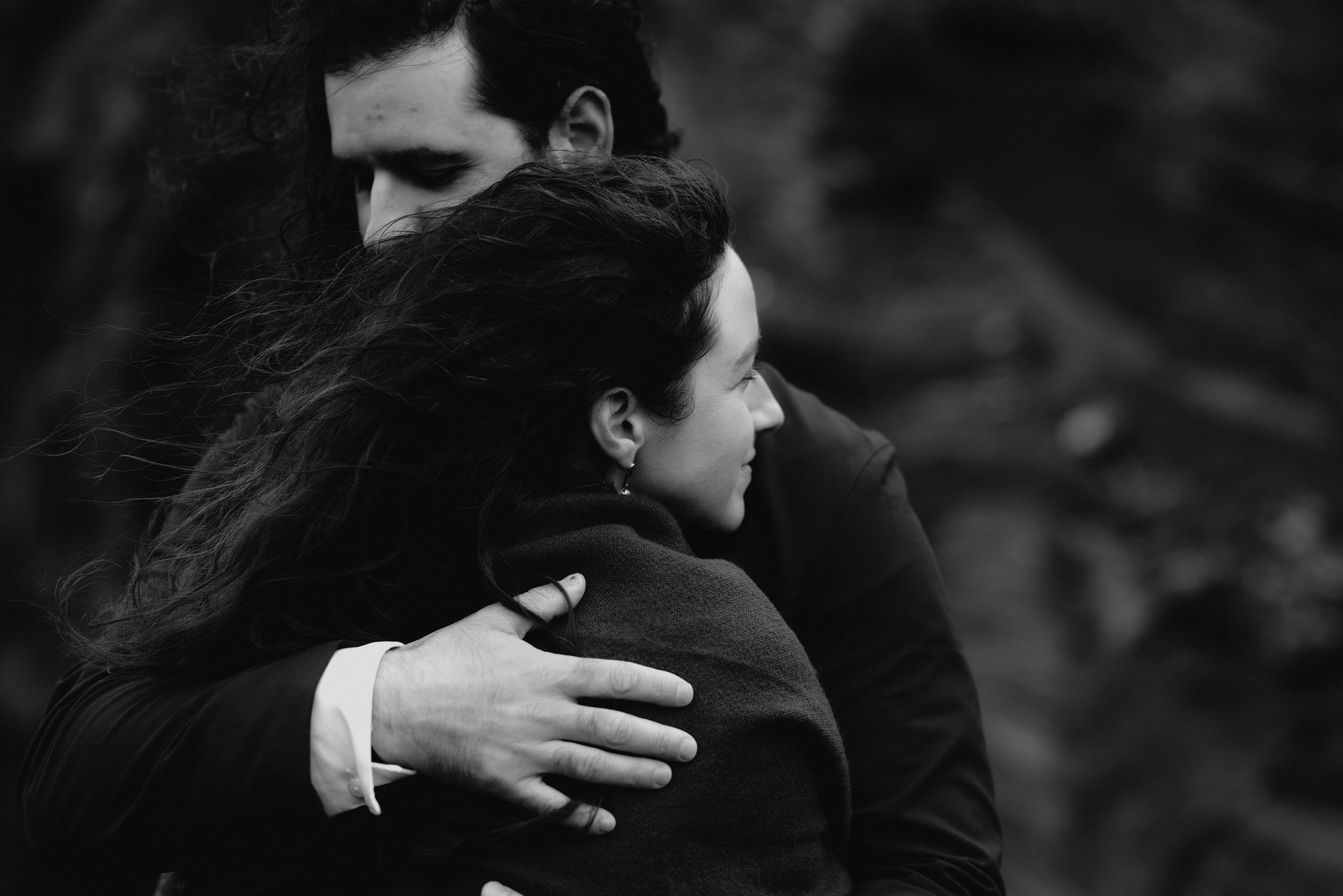 Bride and groom looking out over the vast, mysterious waters of Kleifarvatn, their wedding outfits contrasting against the dark landscape.