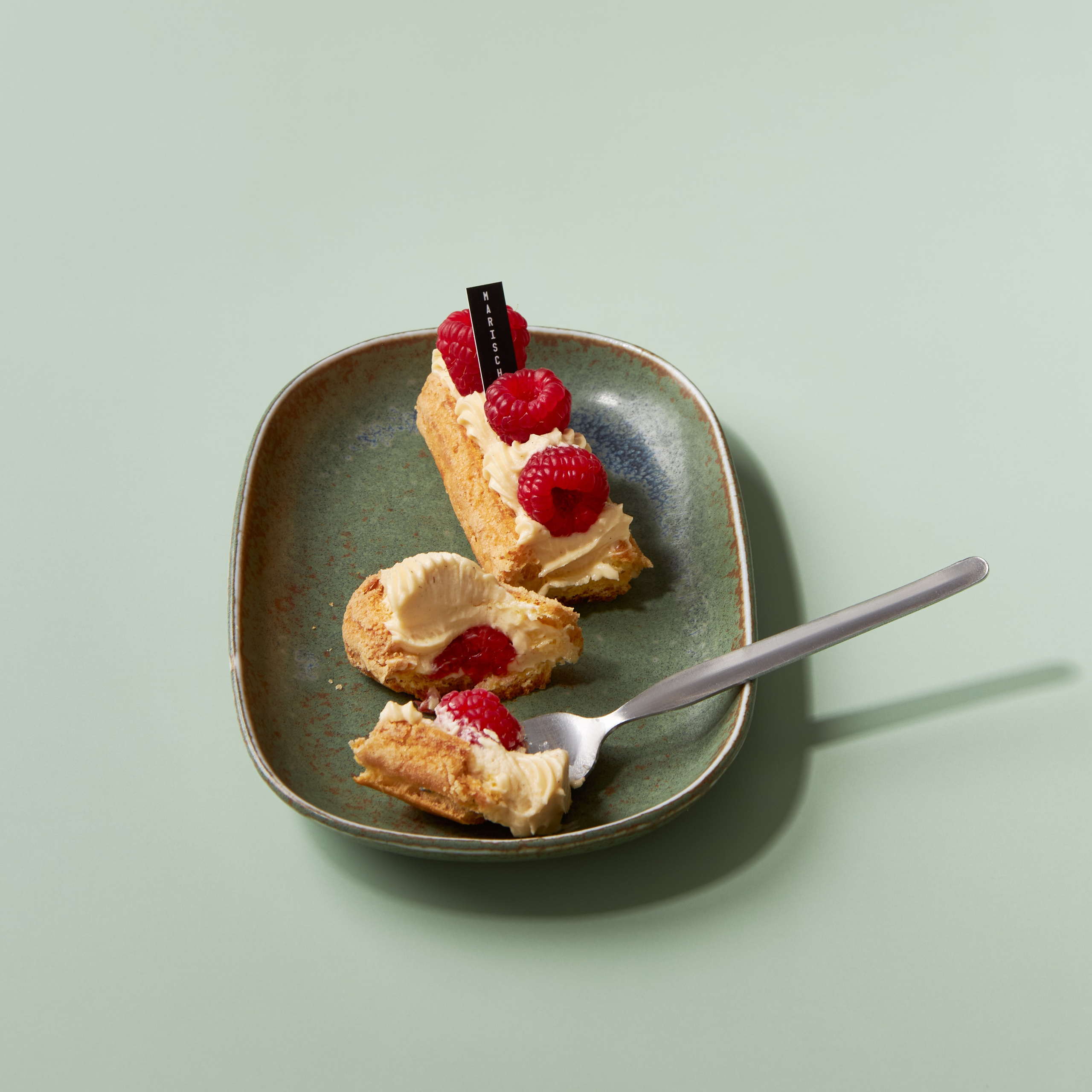 Lifestyle-Foto eines Eclairs mit Himbeere, gebrochen auf Teller, Content-Fotografie für Social Media, Werbung und Banner