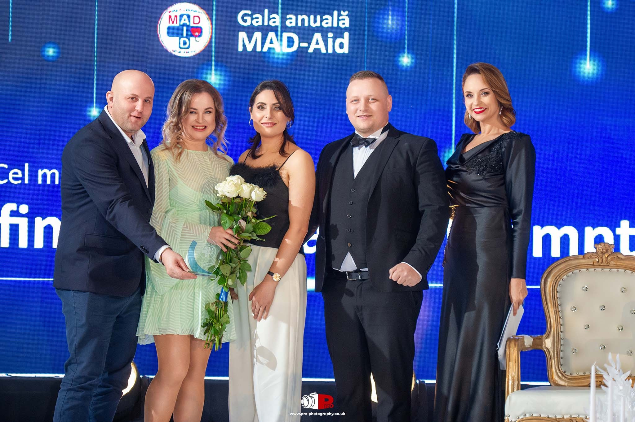  A group of elegantly dressed individuals posing with awards and roses at the MAD-Aid Gala.