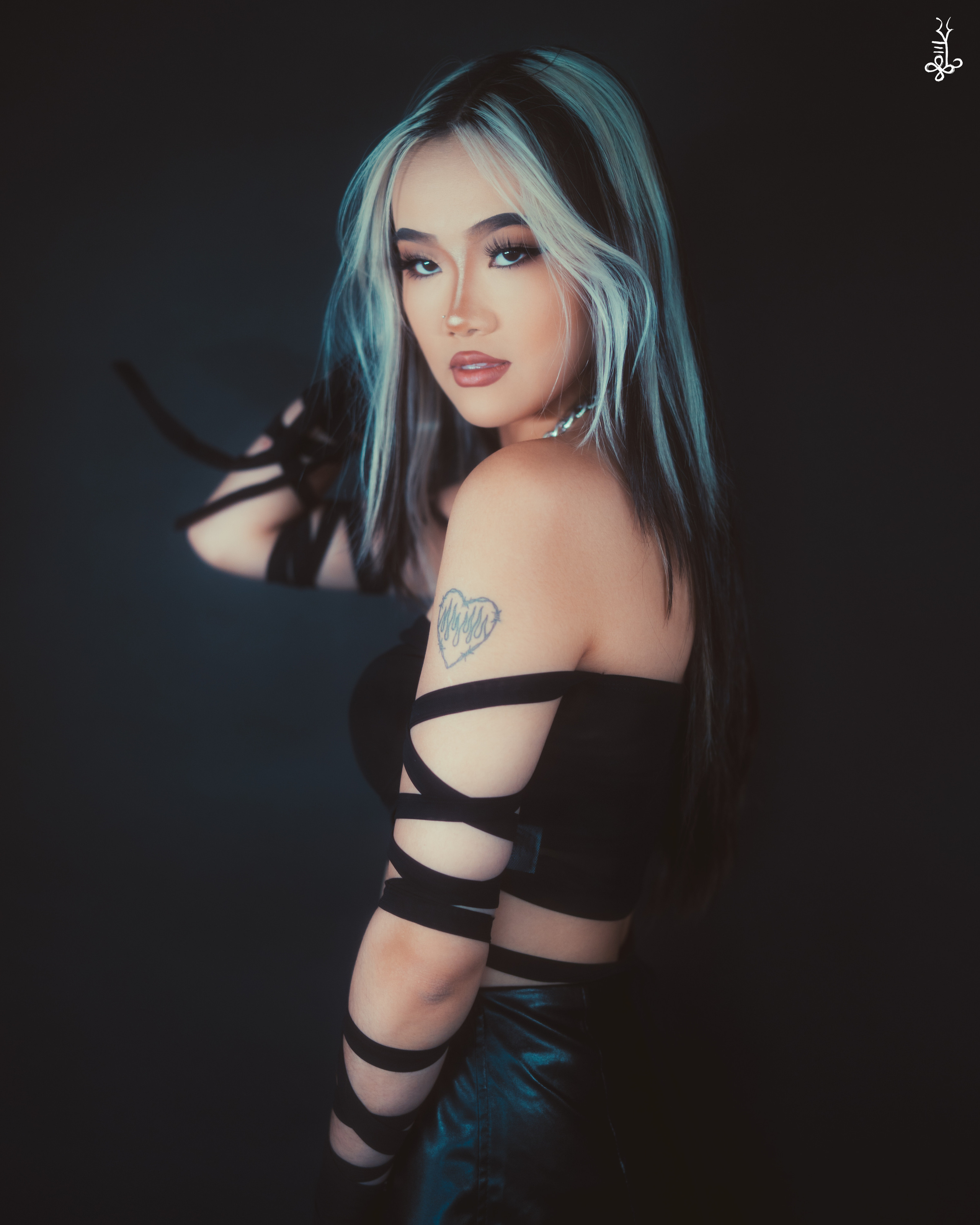 Model in off-shoulder black outfit with piercing gaze, holding strand of turquoise hair