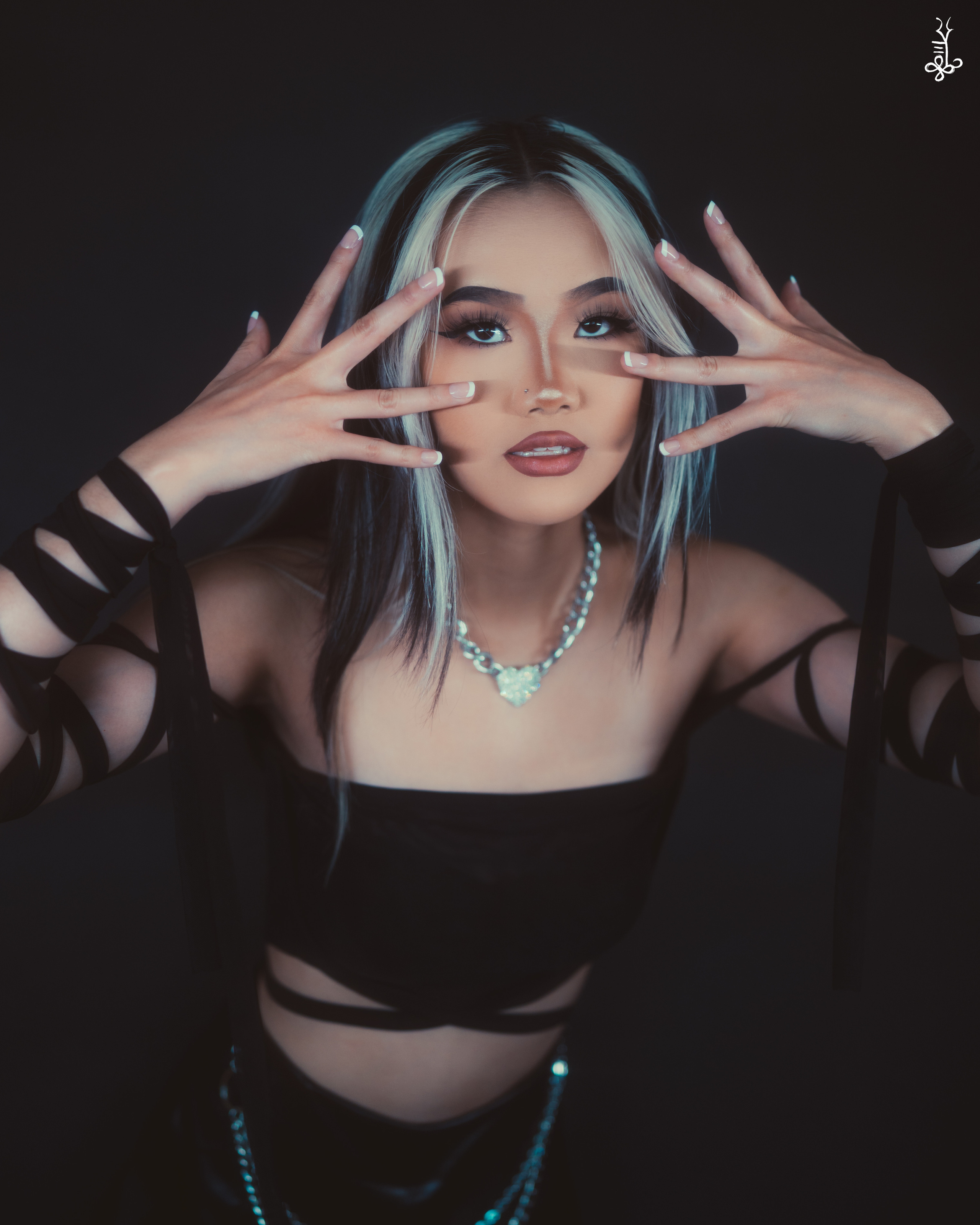 Model with hands framing her face, wearing mesh top and intense expression under moody lighting