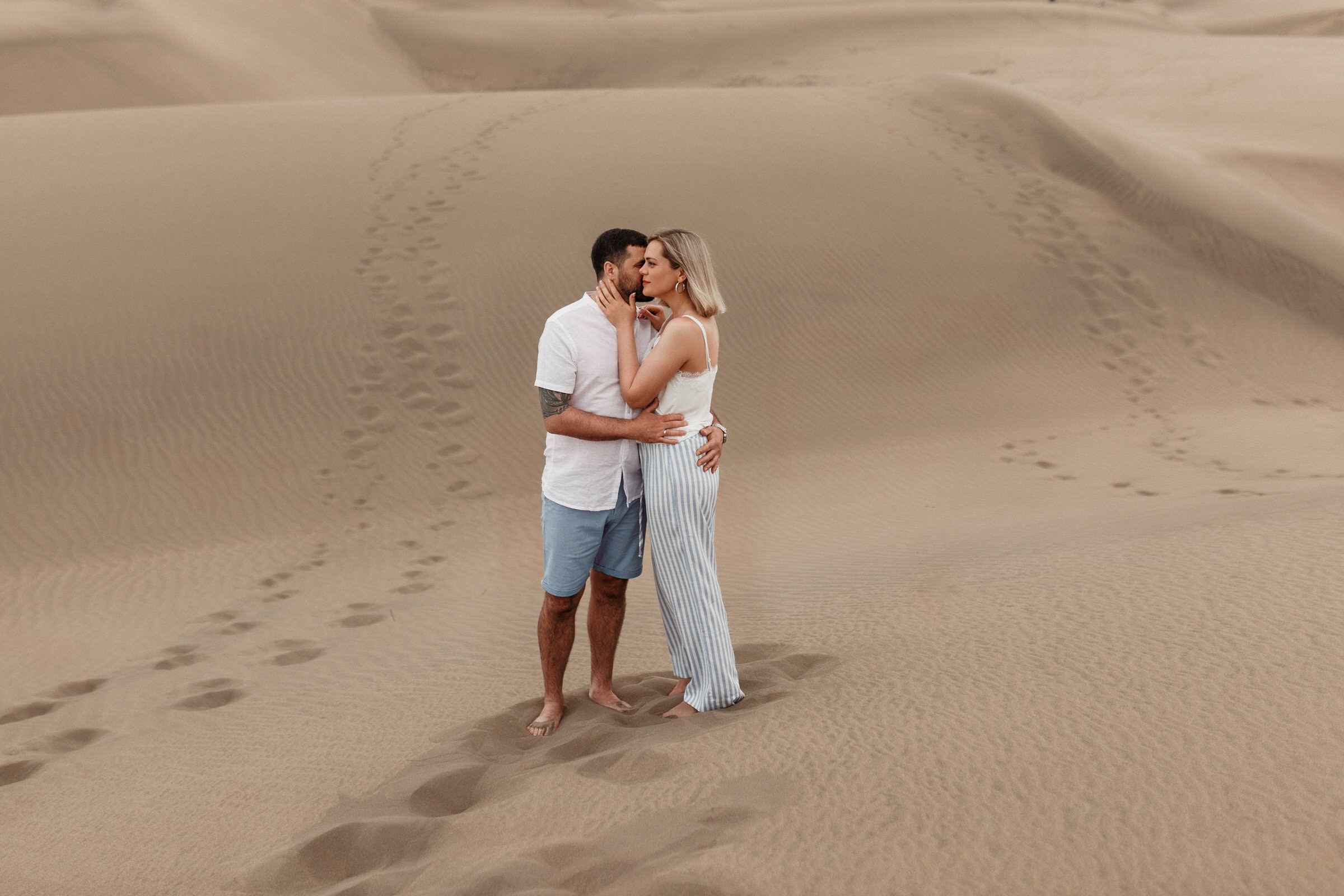 Desert Photographer Maspalomas - A couple embraces and kisses on a vast sandy desert landscape.