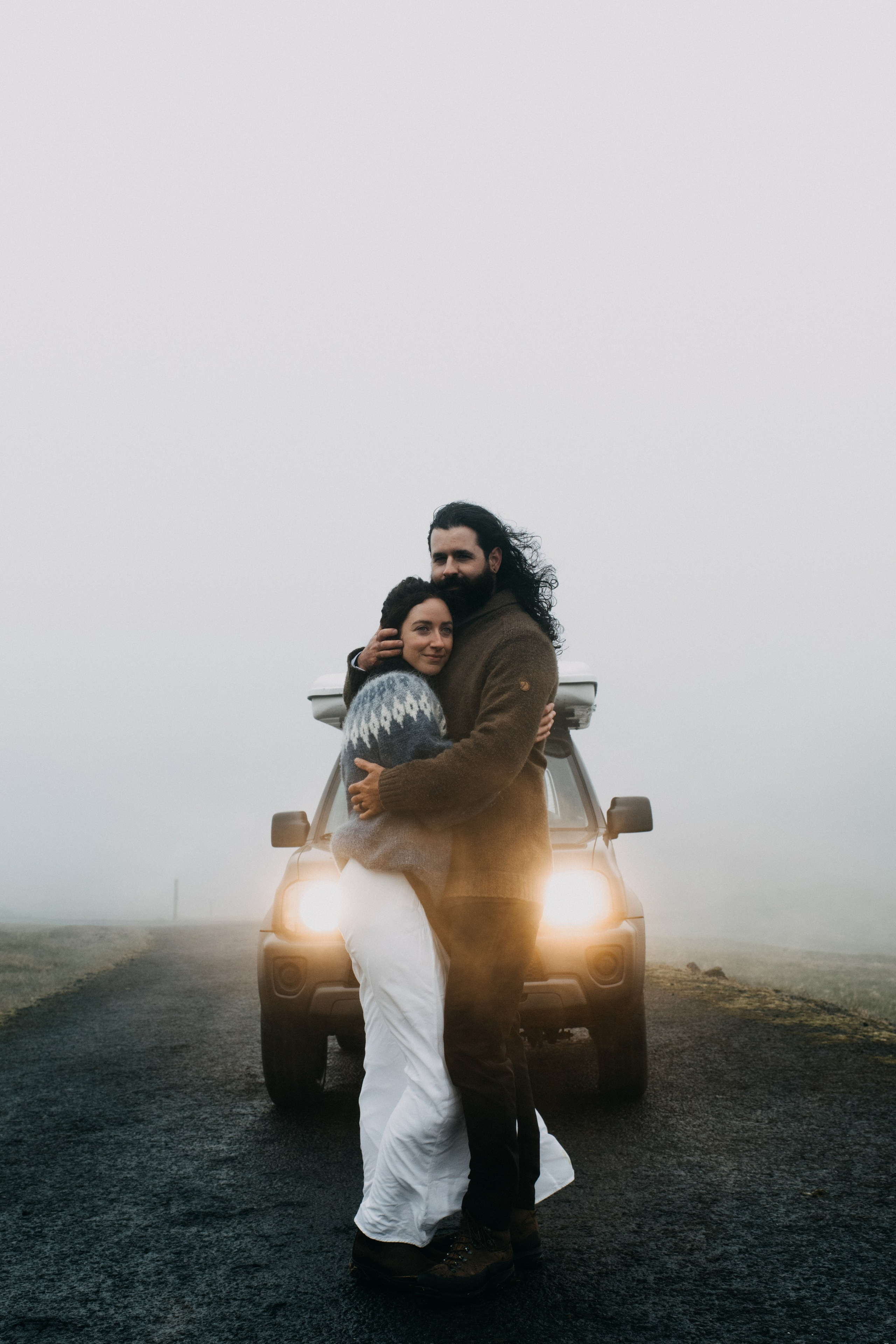 Bride and groom looking out over the vast, mysterious waters of Kleifarvatn, their wedding outfits contrasting against the dark landscape.