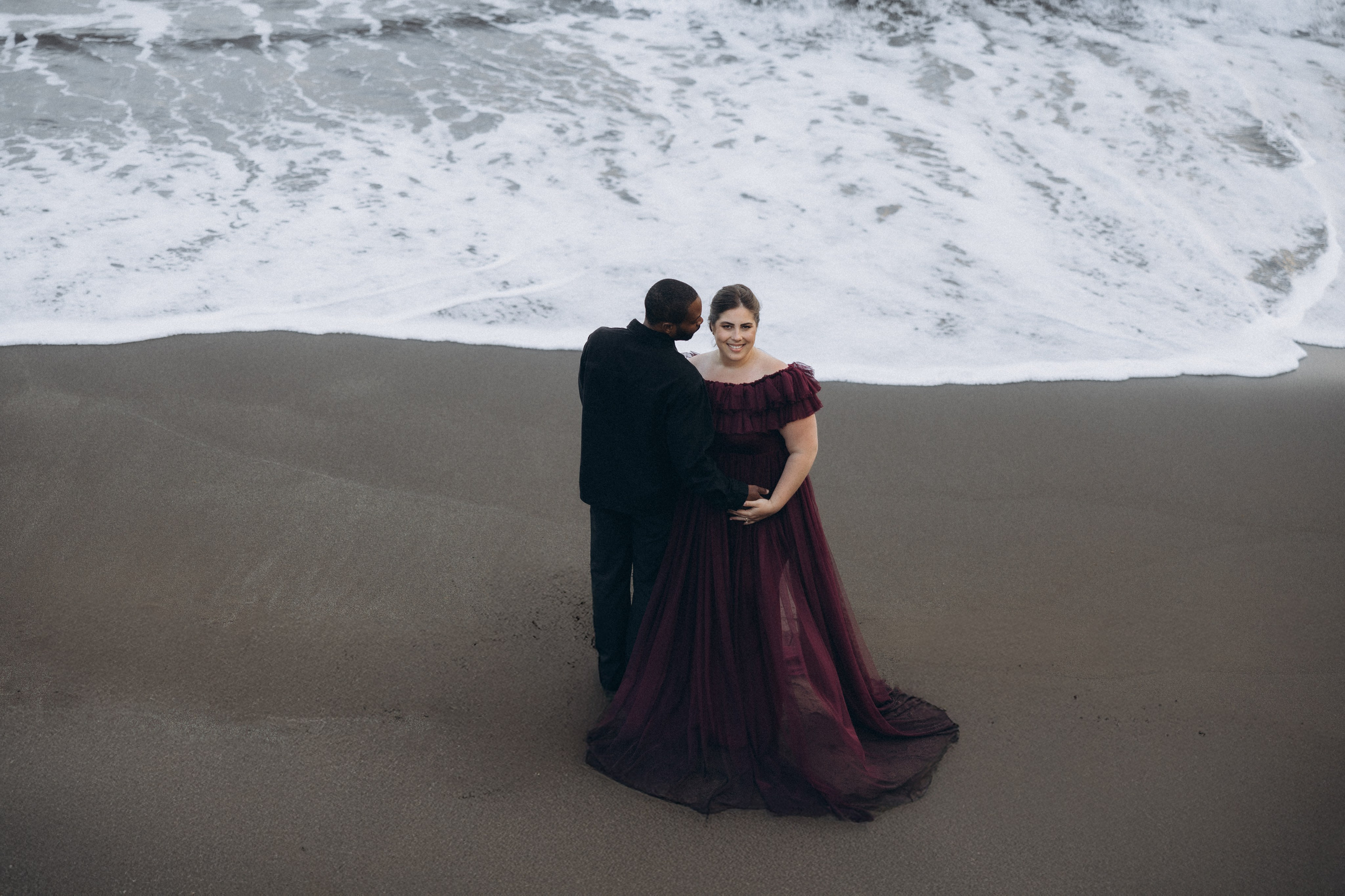 A glowing expectant mother standing on a cliff overlooking the ocean in Madeira, her dress flowing gently in the wind as the golden sunset casts a warm glow.
