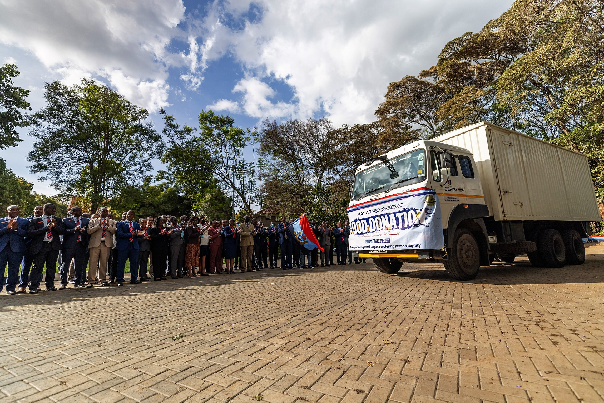 A wide shot of executives and a lorry with a banner on food donations being flagged off, in Nairobi. Documentary storytelling