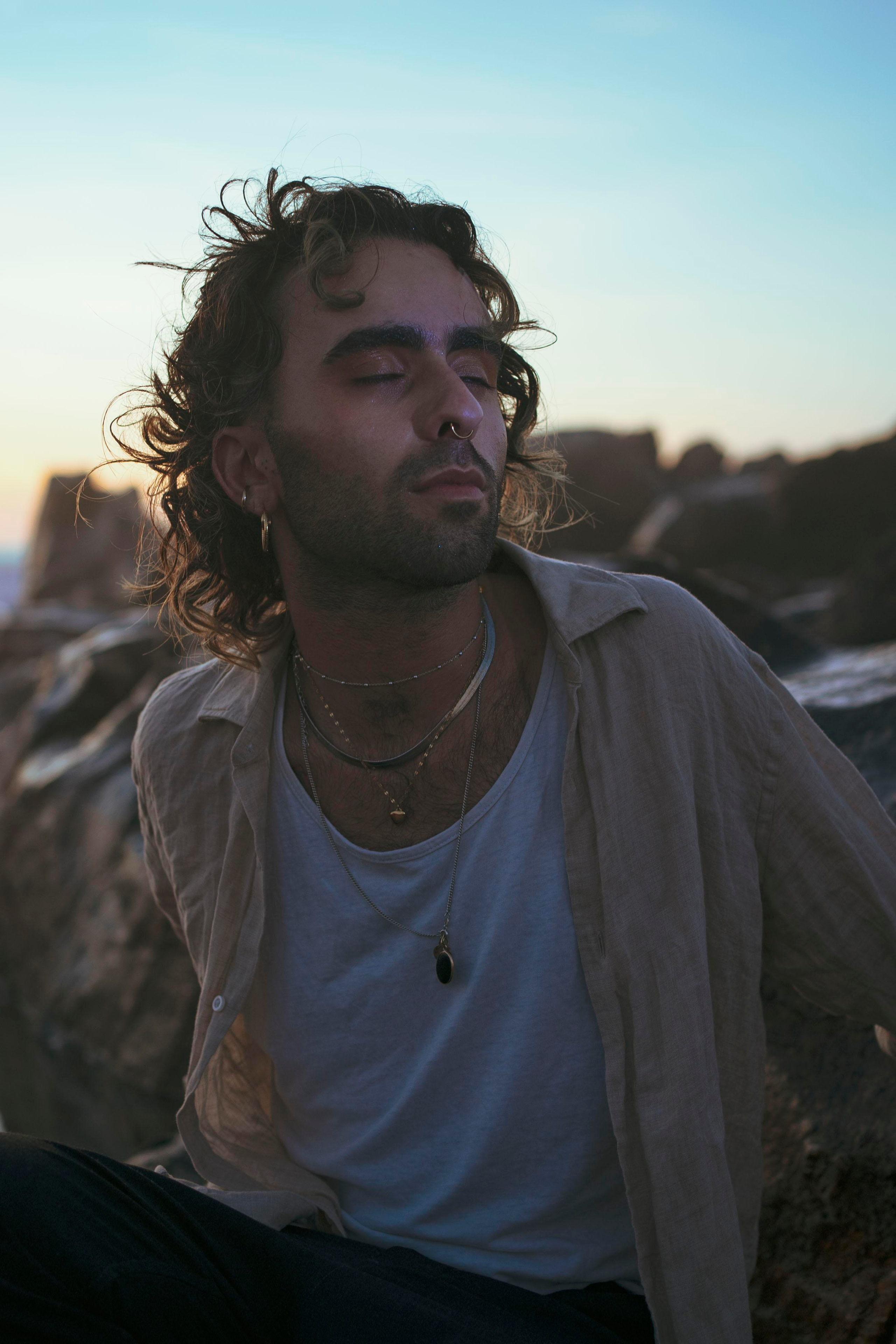 LGBTQ+, LGBT portrait of a beautiful person with makeup, a white tank top, and curly hair. Sunset on a beach, colored light.