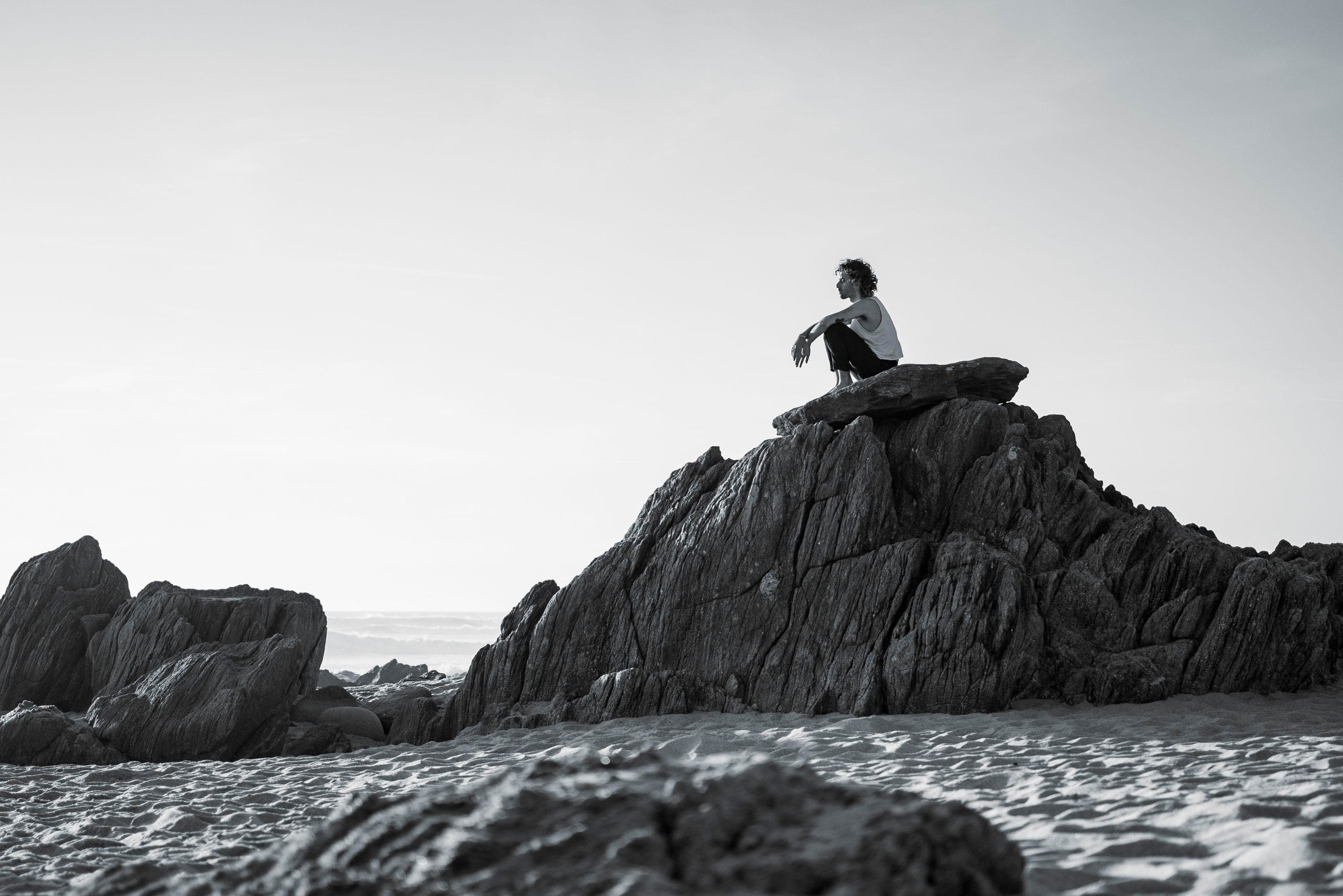 Black and white silhouette of a person sitting on a rock. 