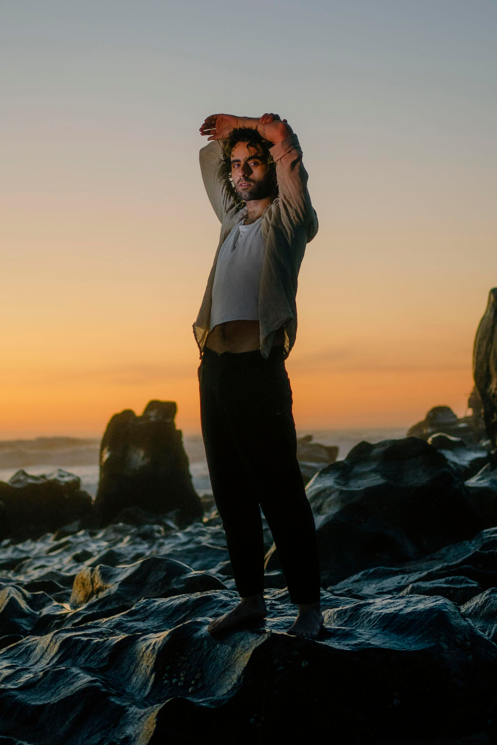 LGBTQ+, LGBT portrait of a beautiful person with makeup, a white tank top, and curly hair. Sunset on a beach, colored light.