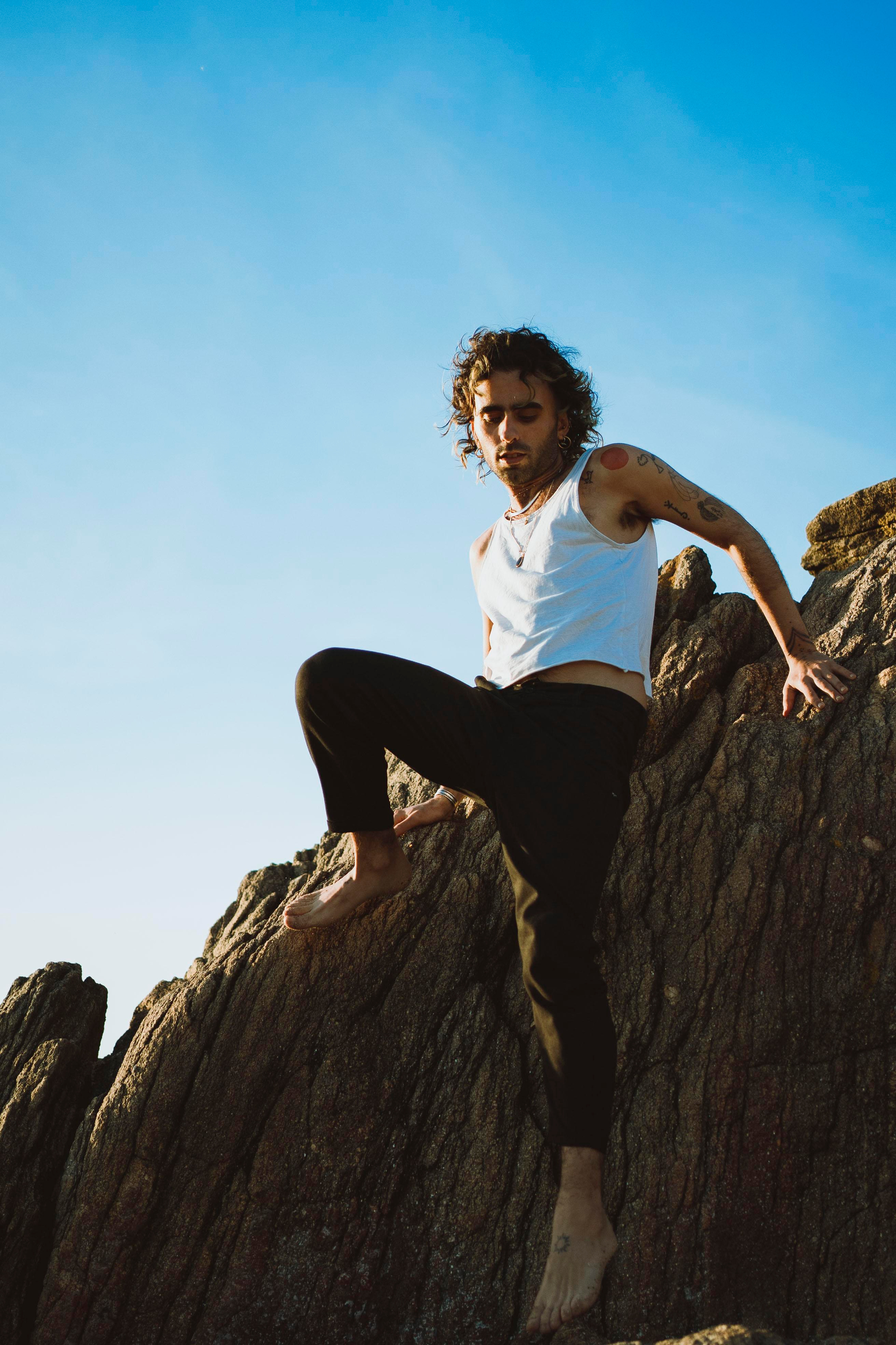 LGBTQ+, LGBT portrait of a beautiful person with makeup, a white tank top, and curly hair. Climbing on a rock.