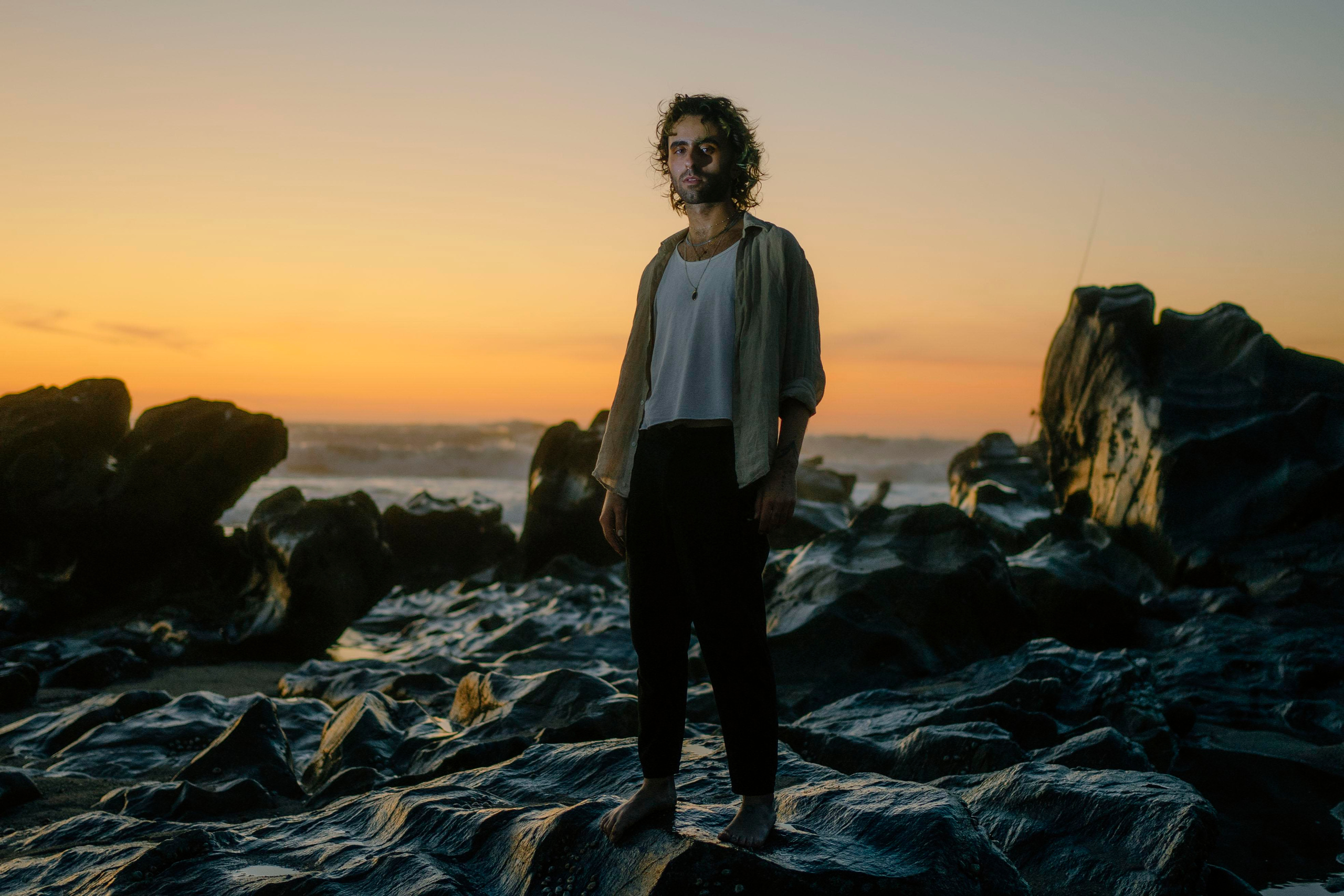 LGBTQ+, LGBT portrait of a beautiful person with makeup, a white tank top, and curly hair. Sunset on a beach, colored light.