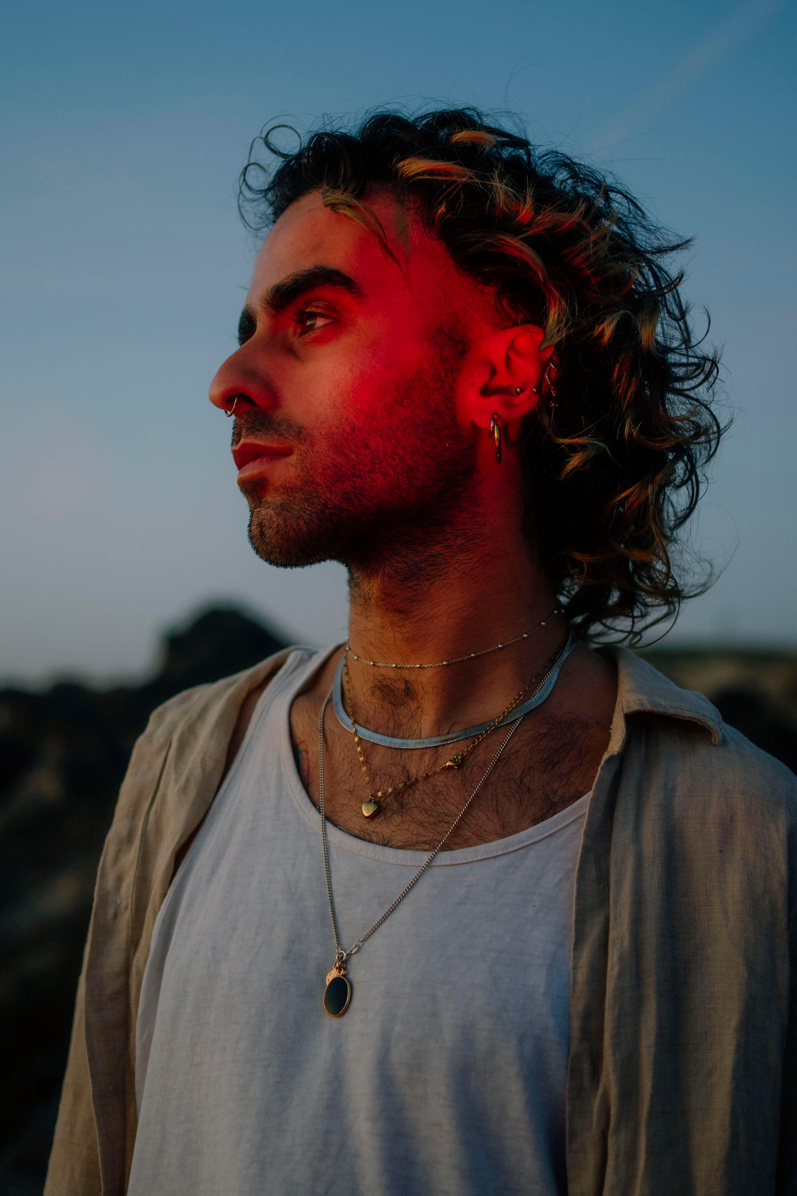 LGBTQ+, LGBT portrait of a beautiful person with makeup, a white tank top, and curly hair. Sunset on a beach, colored light.