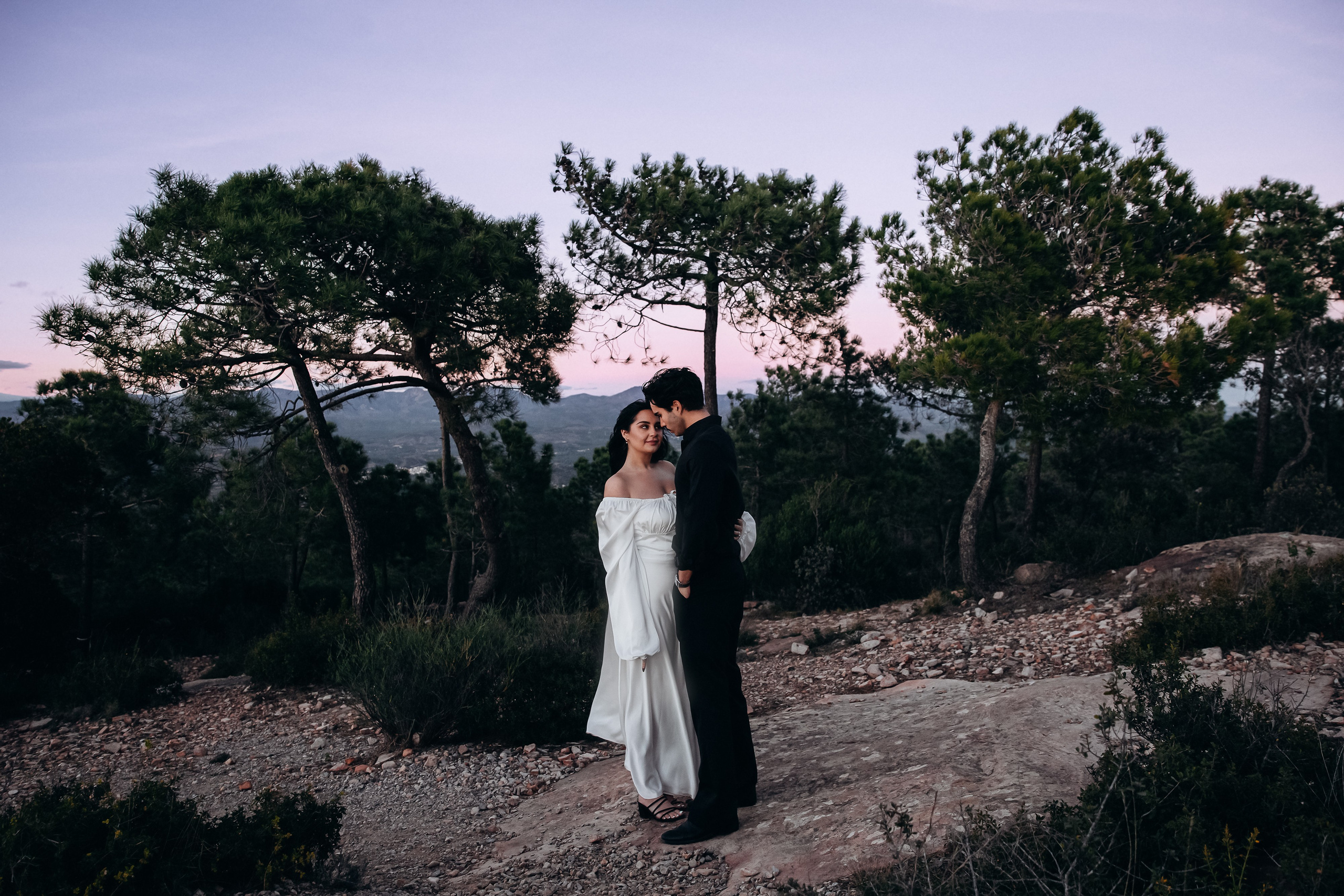 Engagement photoshoot in València, Spain, featuring a couple standing close together among Mediterranean pine trees at golden hour, capturing a quiet, romantic moment in nature with soft light and earthy tones — ideal for engagement photography, elopements, and natural wedding story photoshoots in València and across Spain.