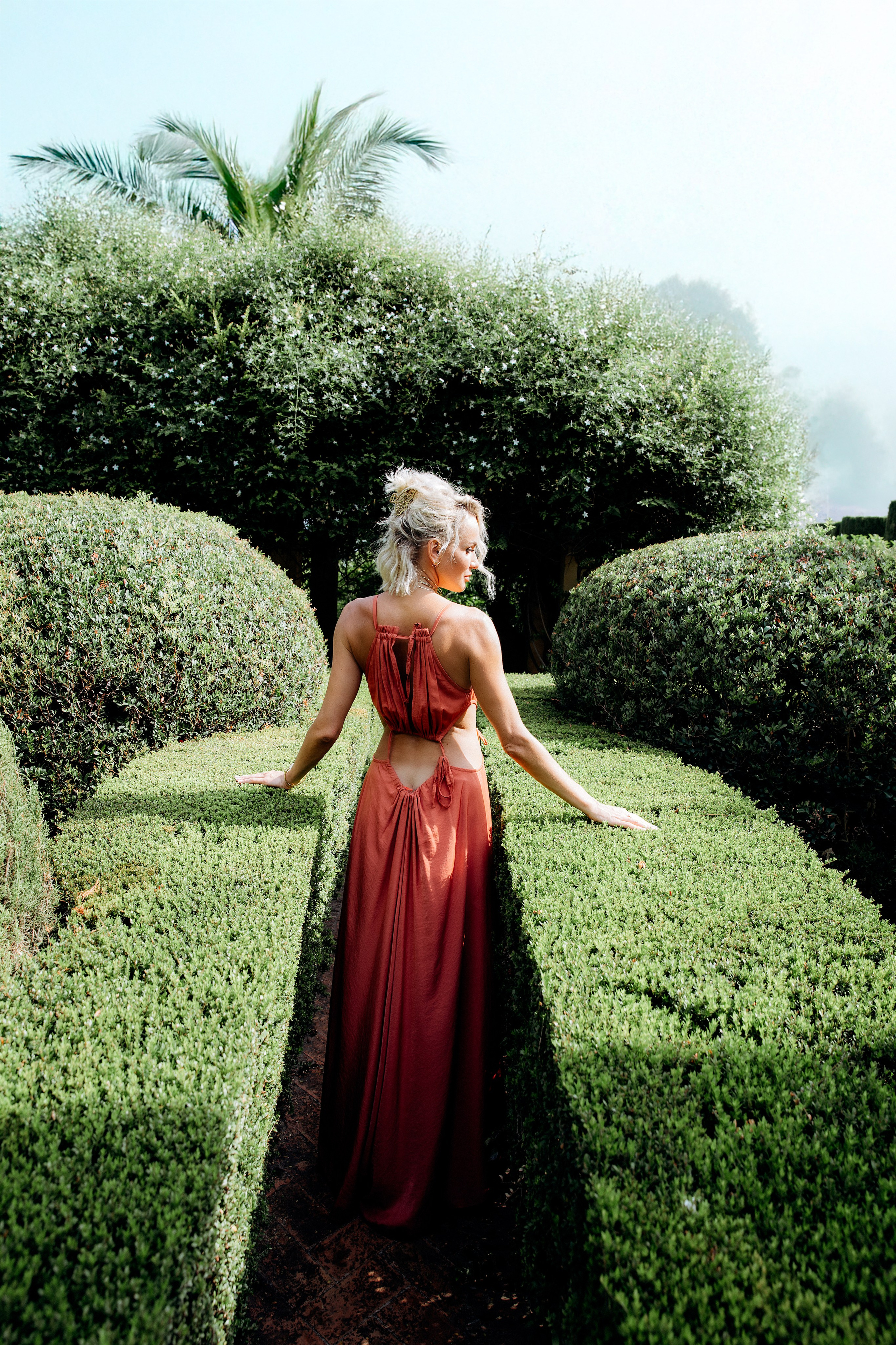 Элегантный портрет женщины в красном платье среди подстриженных кустов в саду в Толедо, Испания. Идеальное вдохновение для стильной и утончённой портретной фотосессии в Толедо и других городах Испании.