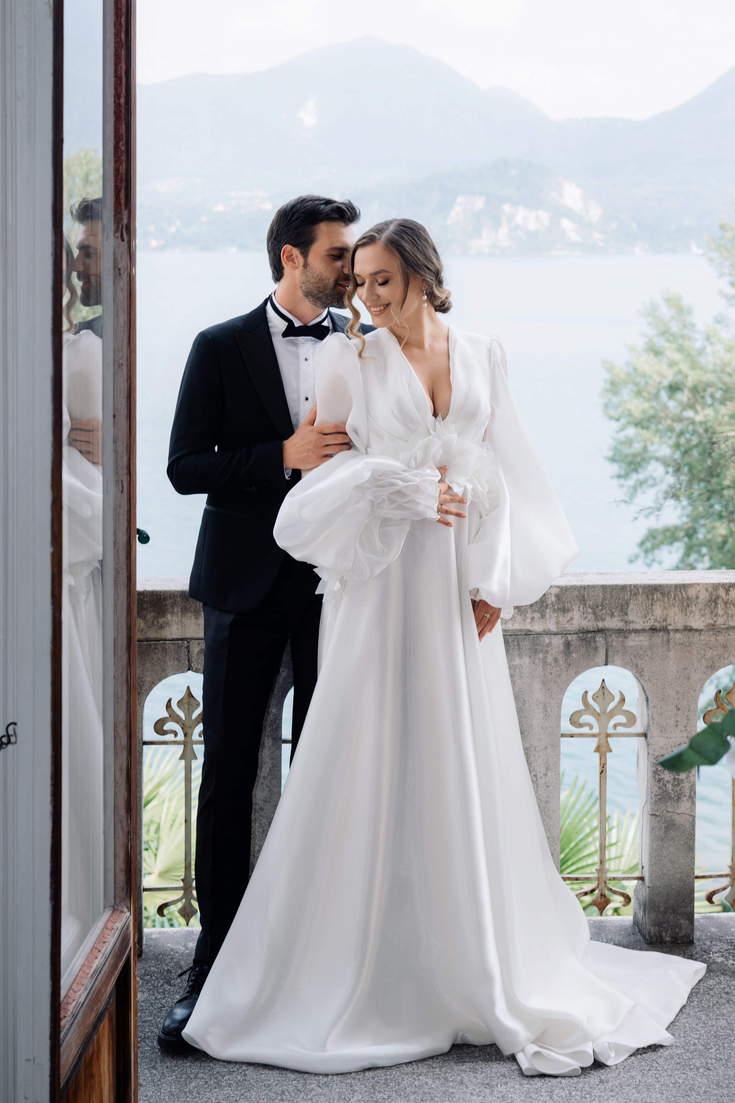 a bride and groom pose for a photo in front of the lake comoo