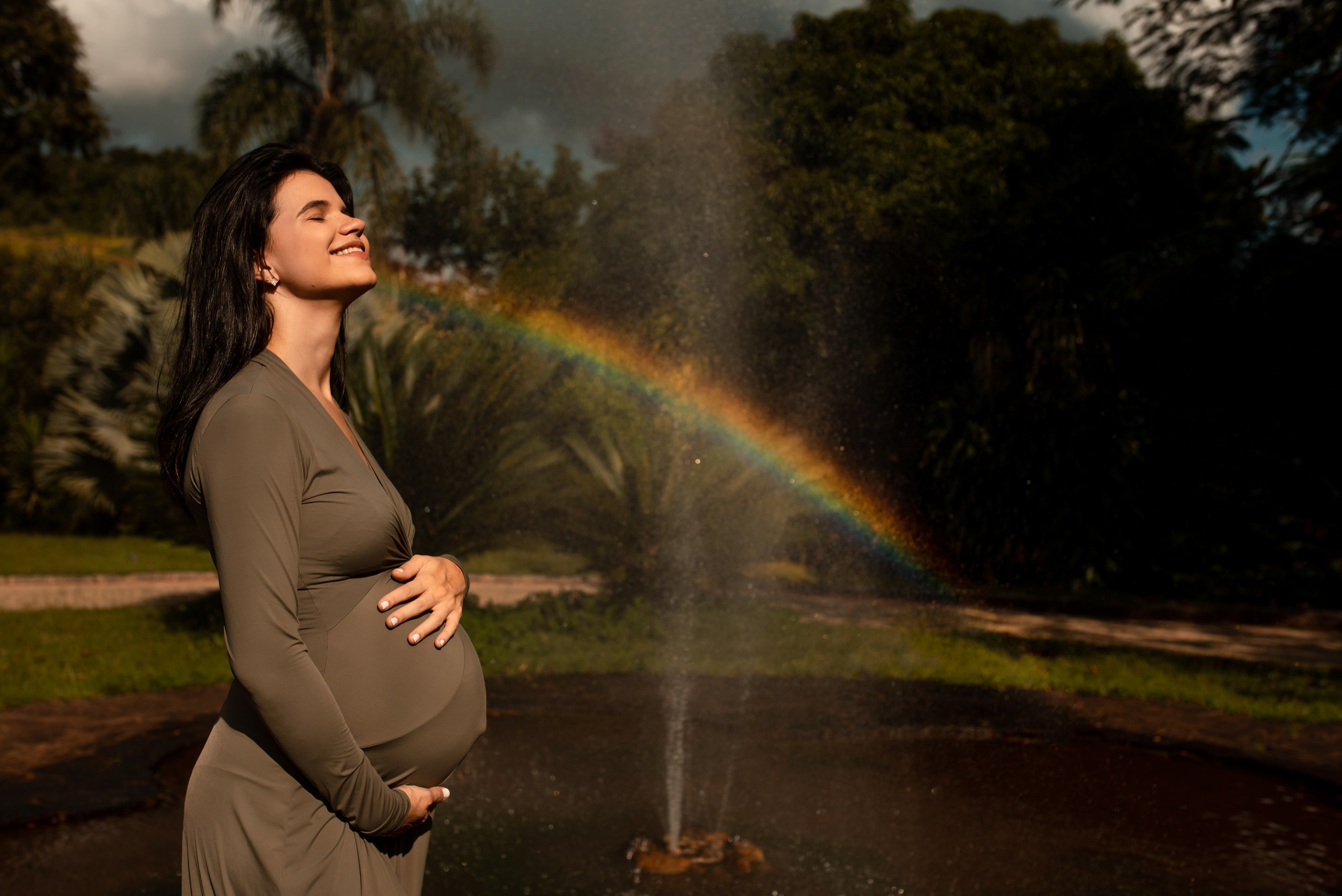 Ensaio gestante ao ar livre em Juiz de Fora, mãe grávida sorrindo com arco-íris natural ao fundo