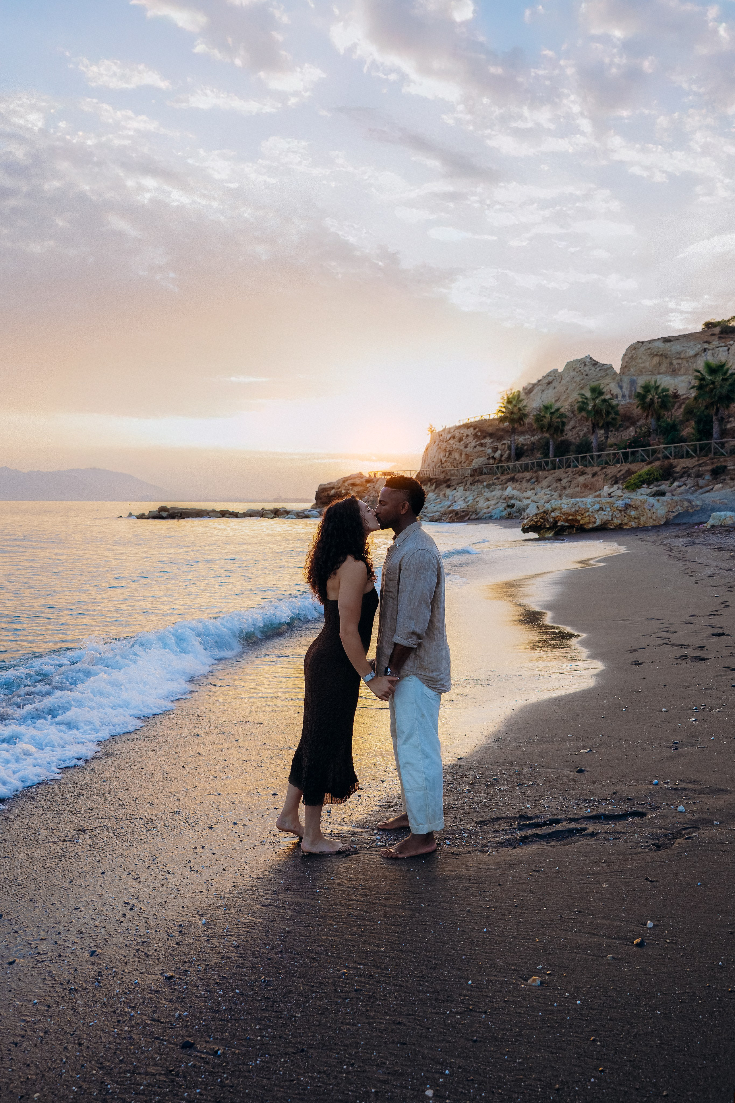 Romantic destination proposal session in Málaga at sunset, with the newly engaged couple standing barefoot by the shoreline. Warm Mediterranean light enhances this intimate engagement shoot on the Costa del Sol.