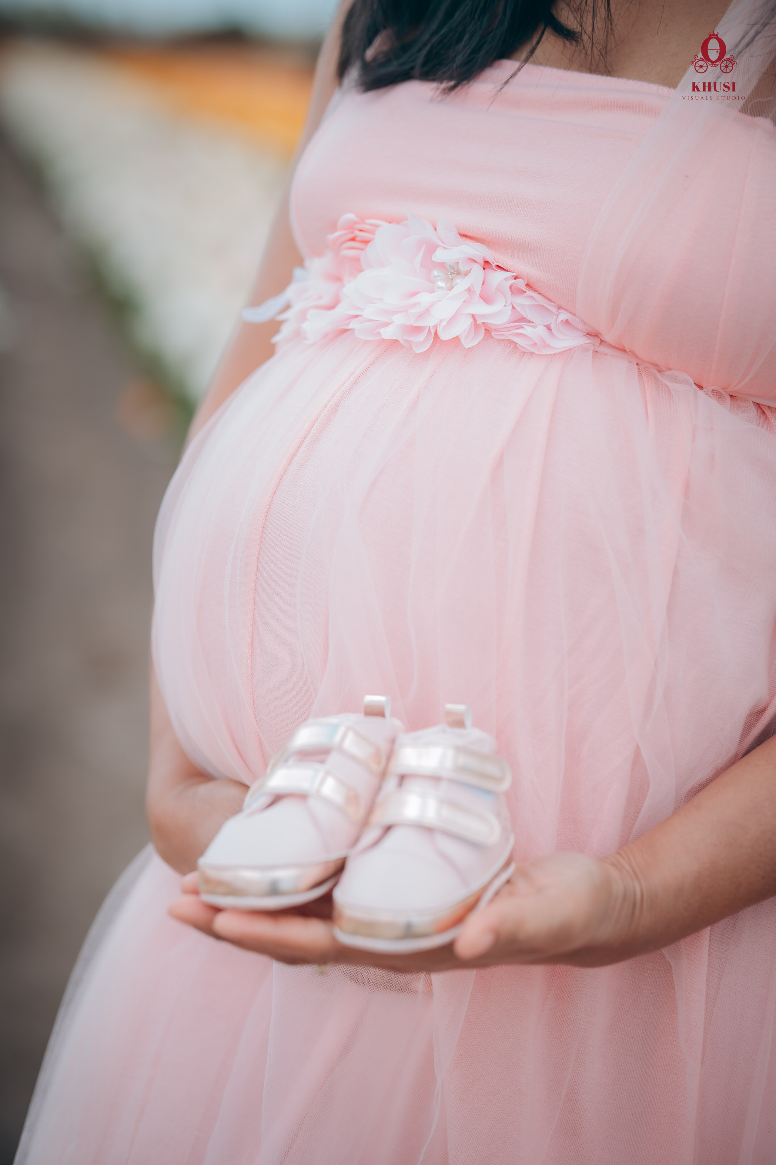 A pregnant mother is holding baby shoes and standing in a tulip flower field in netherlands