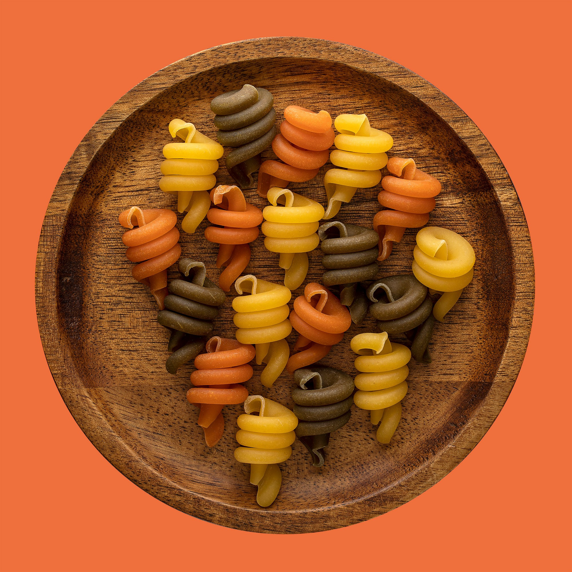 Photographer Roman Djuzev - Trottole tricolore pasta on a wooden plate, shot in high key, on a white background.