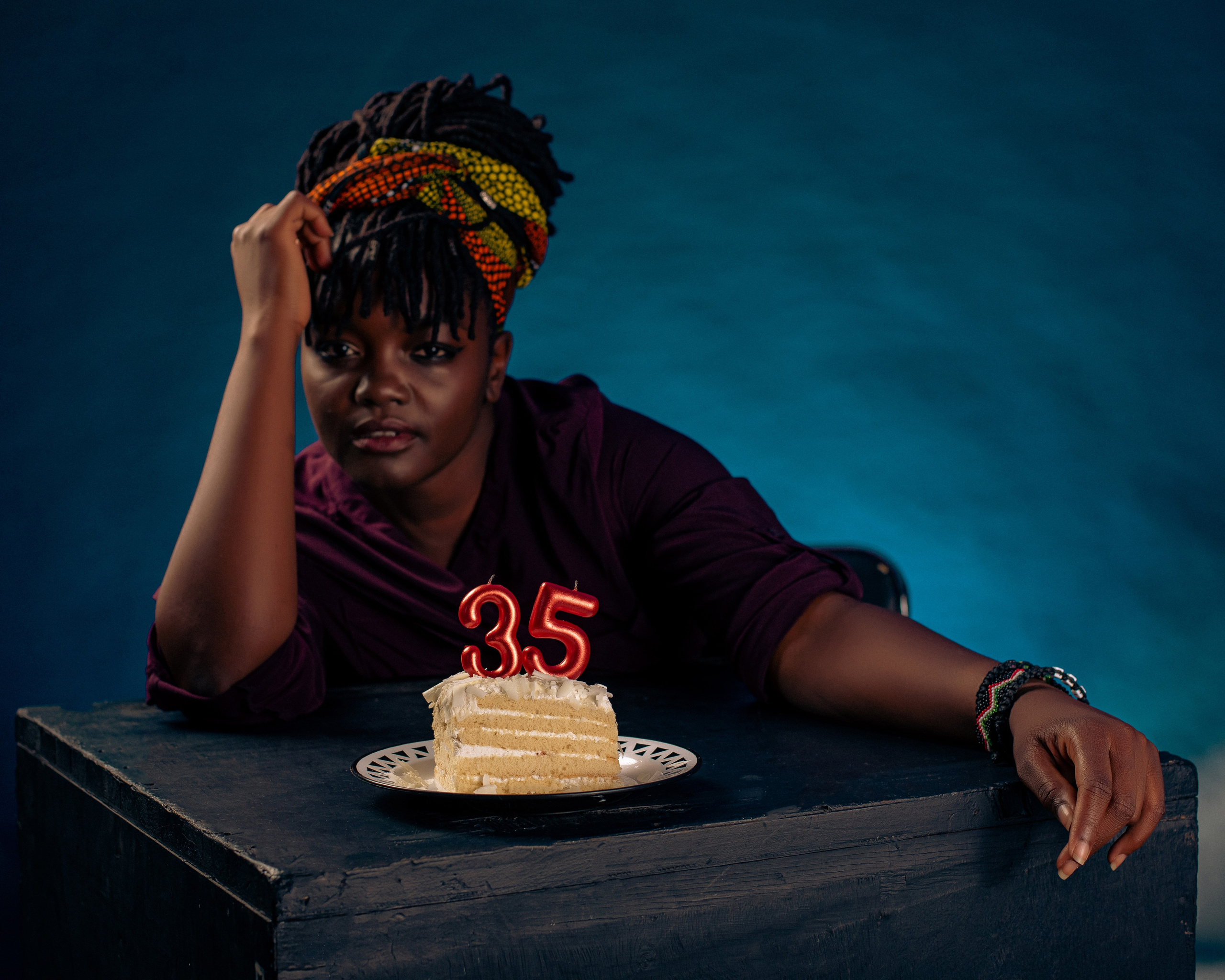 Young woman in ankara headwrap resting on table with a birthday cake— creative studio portrait by Nick Ouma Photography, Kenya