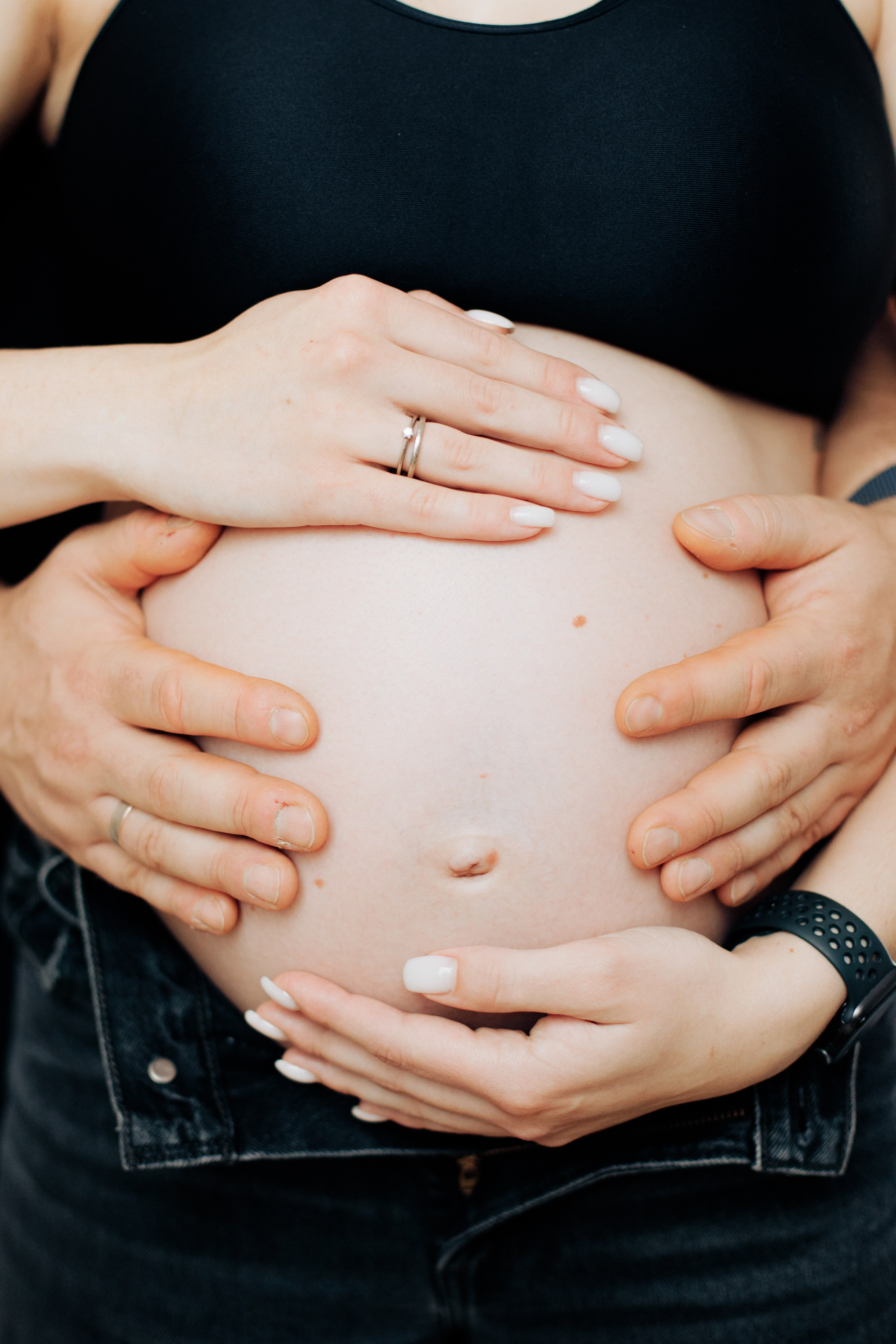 Hände von Mutter und Vater liegen gemeinsam auf dem Babybauch.