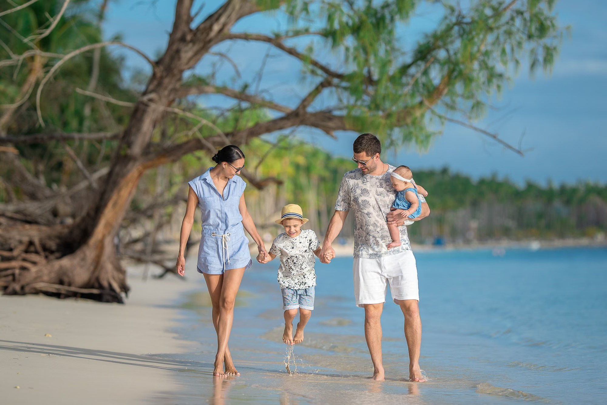Parents holding their children while walking along a tropical beach in Punta Cana.