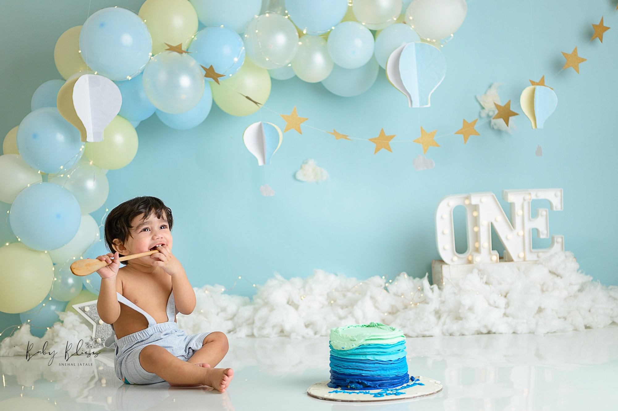 blue white balloon arch in background and child enjoying blue cake in a dreamy cake smash setup.