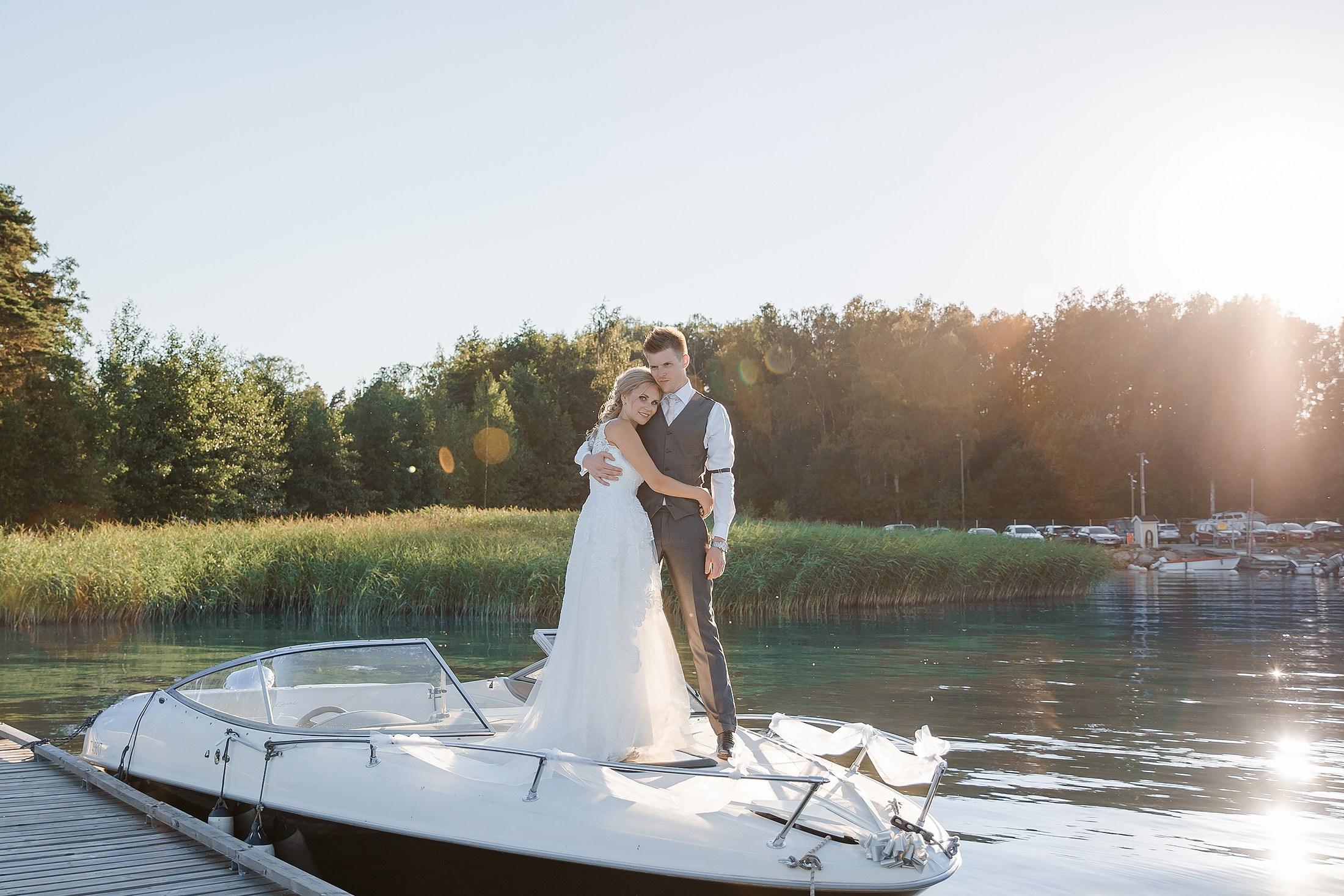 Hääpari seisoo veneen nokassa auringonlaskussa