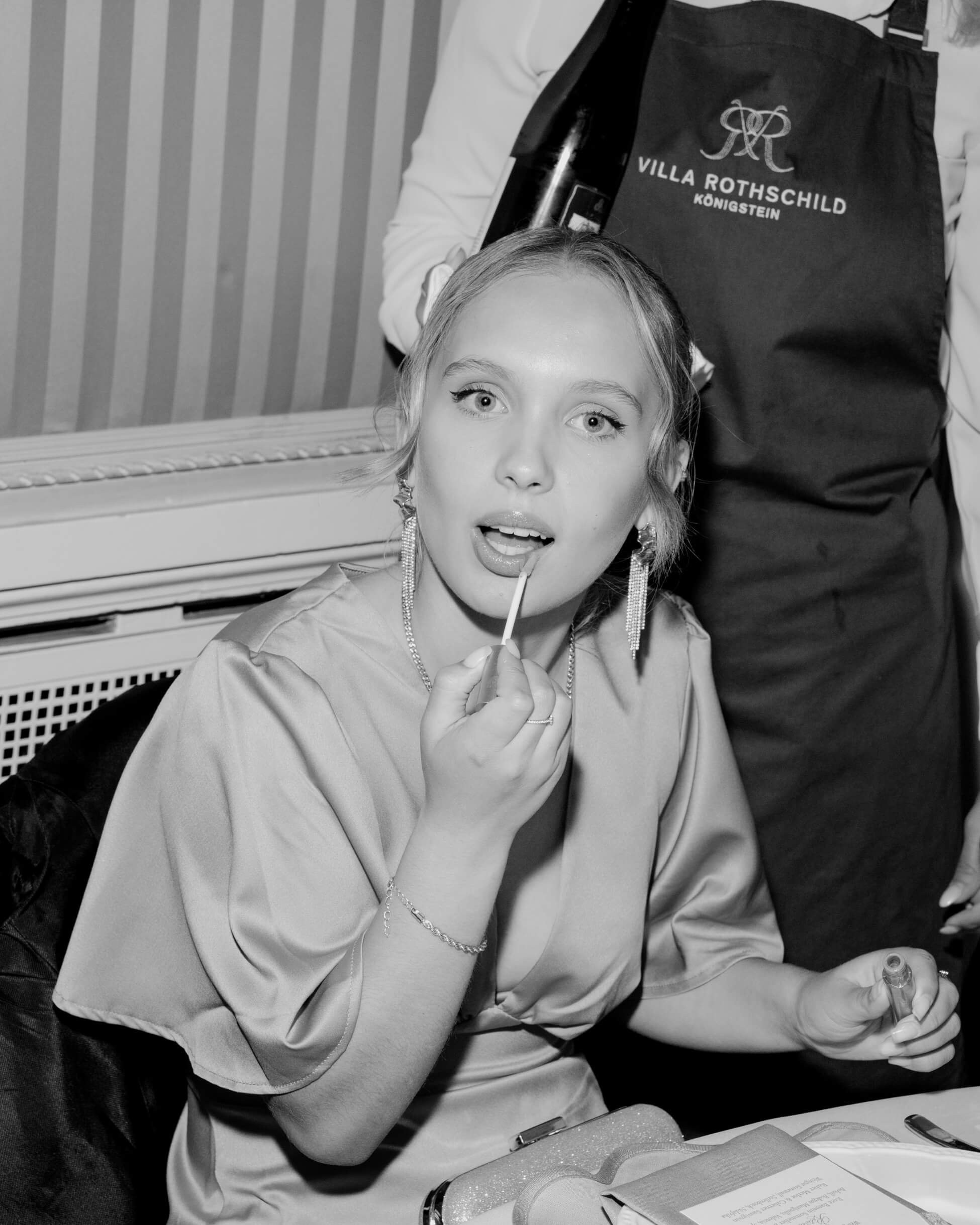 Wedding guest in formal attire put on her lipstick at luxury wedding reception, Villa Rothschild Frankfurt