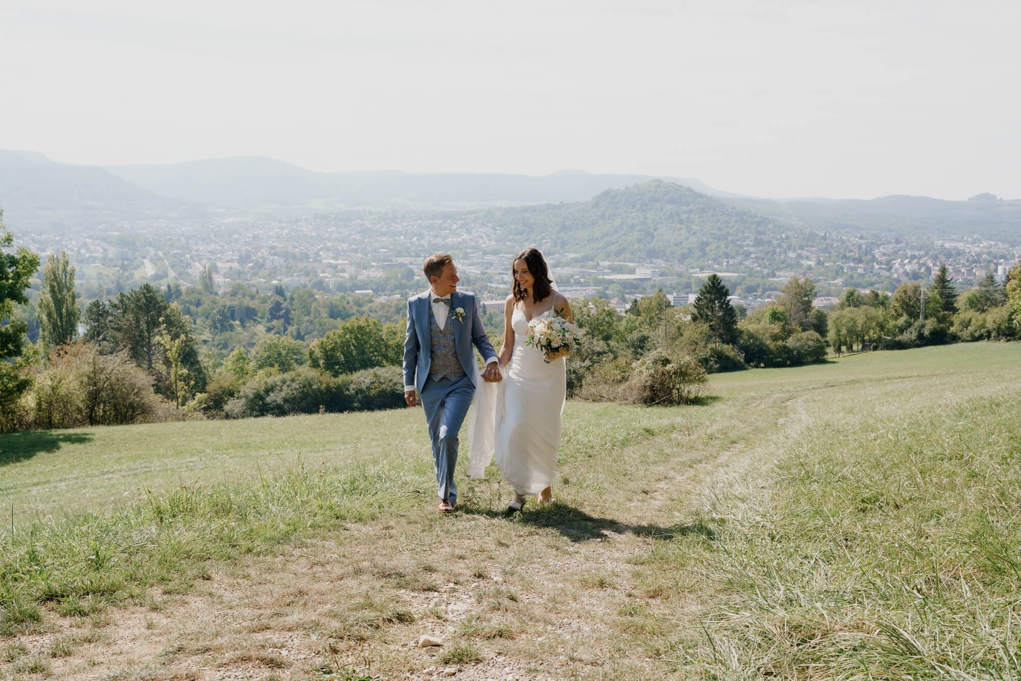 Couple walking hand in hand along a hilltop path with the Stuttgart valley panorama stretching behind them