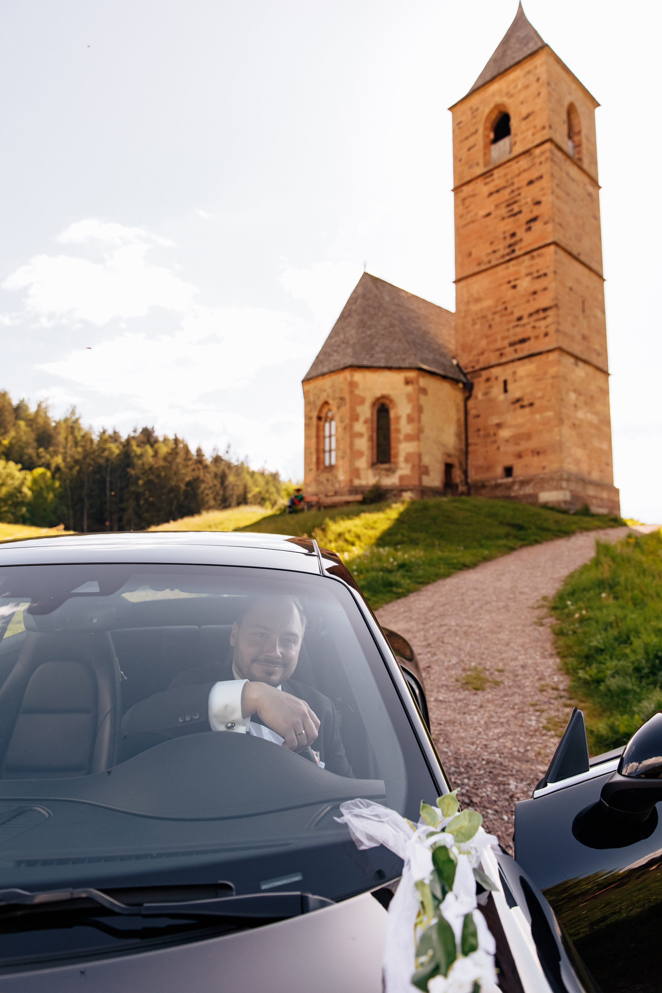Der Bräutigam sitzt in seinem Porsche vor der romantischen Kirche St. Kathrein in Hafling – stilvoller Moment.