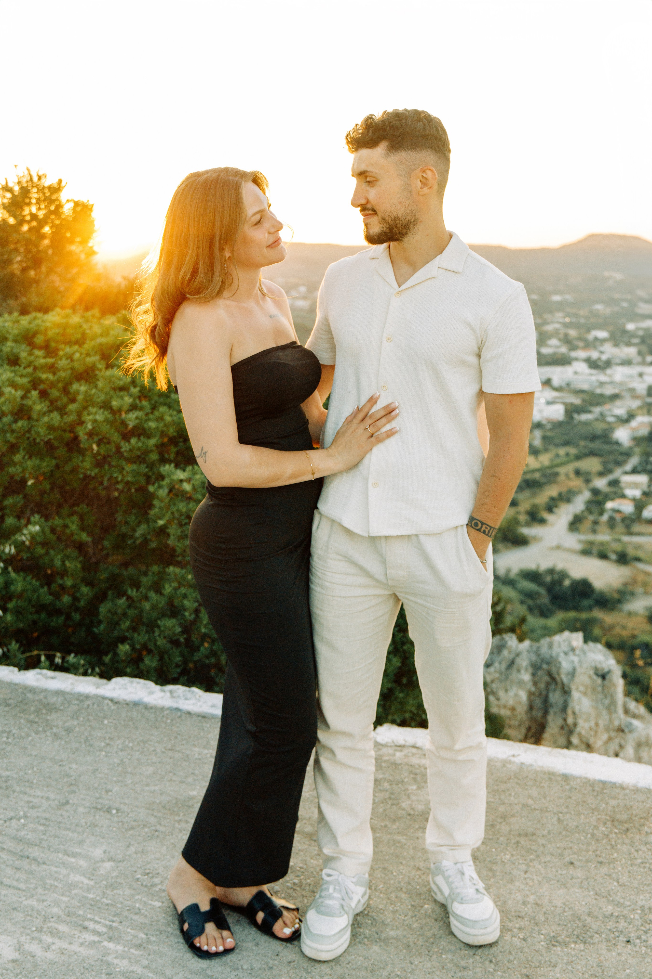 "Liebevoller Blickkontakt: Ein Paar auf dem Felsplateau des Profitis Ilias vor der Kulisse von Faliraki und dem Mittelmeer."