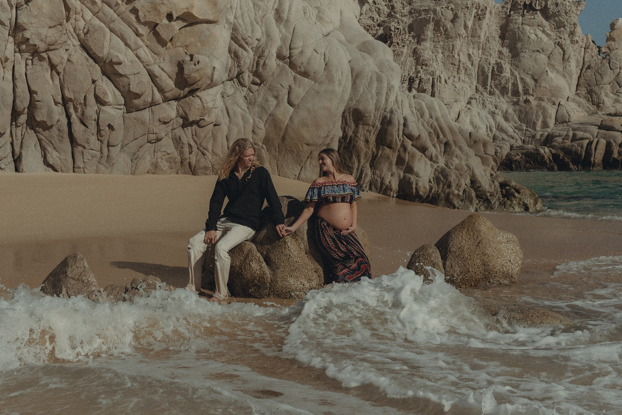 Maternity session in Los Cabos – expecting mother photographed at Playa del Amor with cinematic color grading, warm light, and the iconic Cabo rock formations in the background.