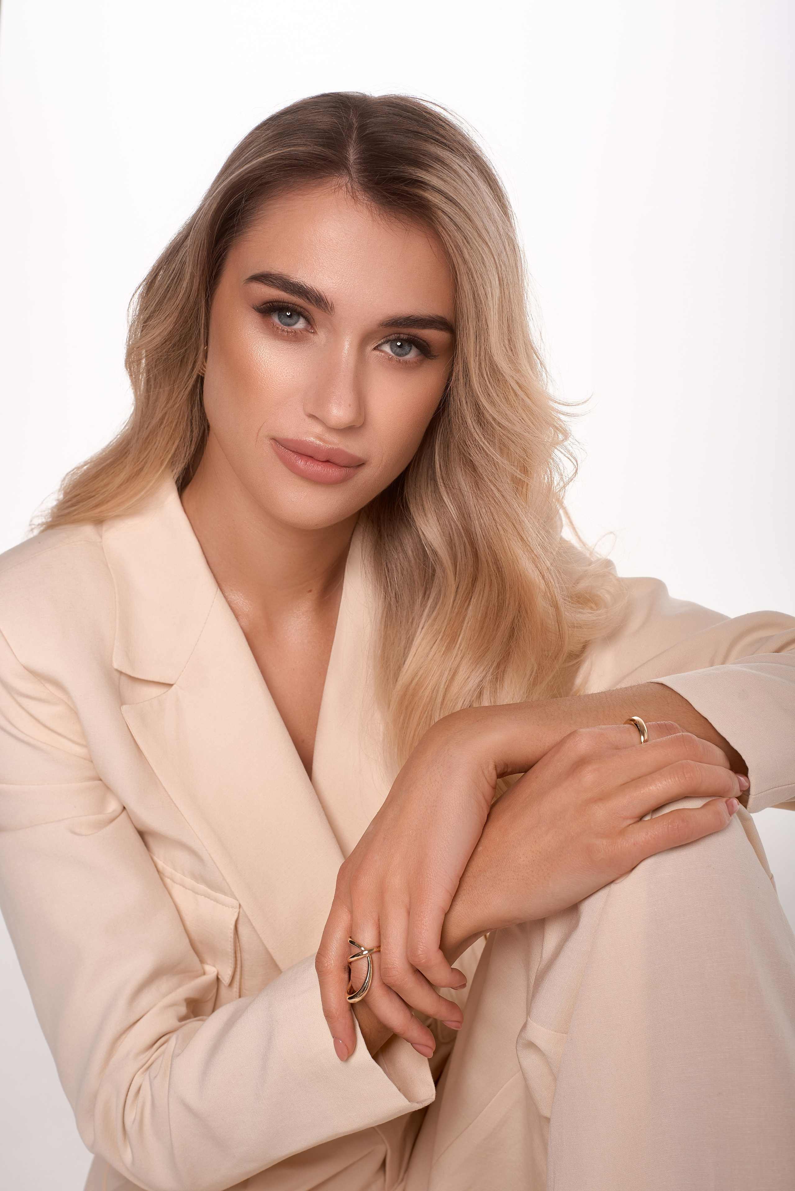 Жіночий портрет у світлому брючному костюмі на білому фоні. Легка хвиляста зачіска та натуральний макіяж підкреслюють природну красу моделі. Діловий, але водночас елегантний образ із м'яким, впевненим поглядом. Золоті прикраси додають вишуканості, а пастельні тони створюють стильний мінімалістичний вигляд. Професійна студійна фотосесія для персонального бренду, бізнес-портрета або іміджевої зйомки.