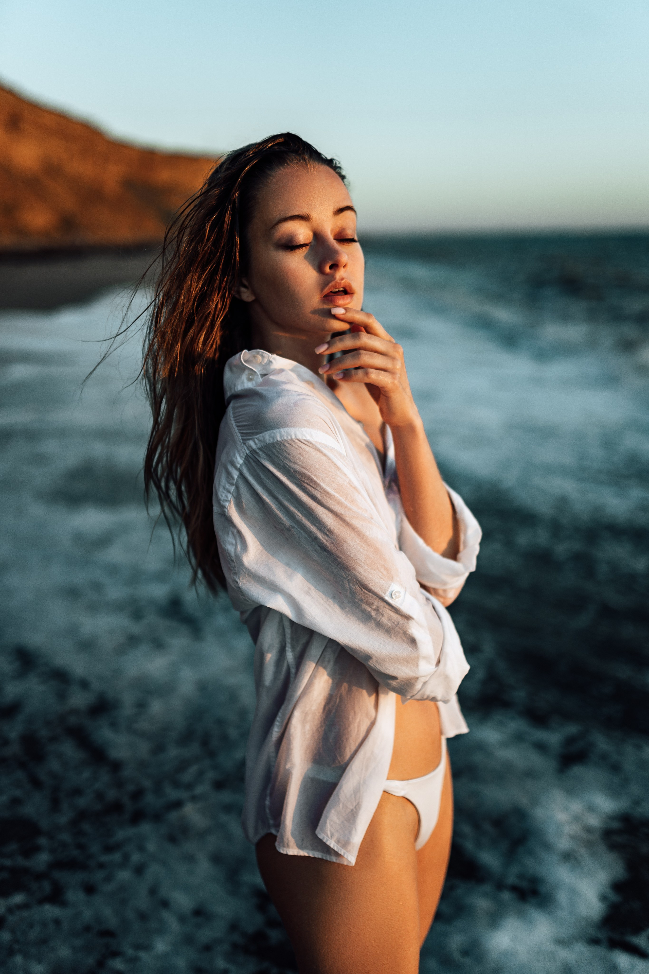 The model stands at the water's edge, wearing a white shirt that contrasts beautifully with the blue ocean and sky. Her thoughtful gaze into the distance embodies a sense of peace and reflection. Capture your own moments like these by booking a session with Miami's top photographer. ocean view, white shirt, thoughtful gaze, peace, reflection, top photographer, Miami