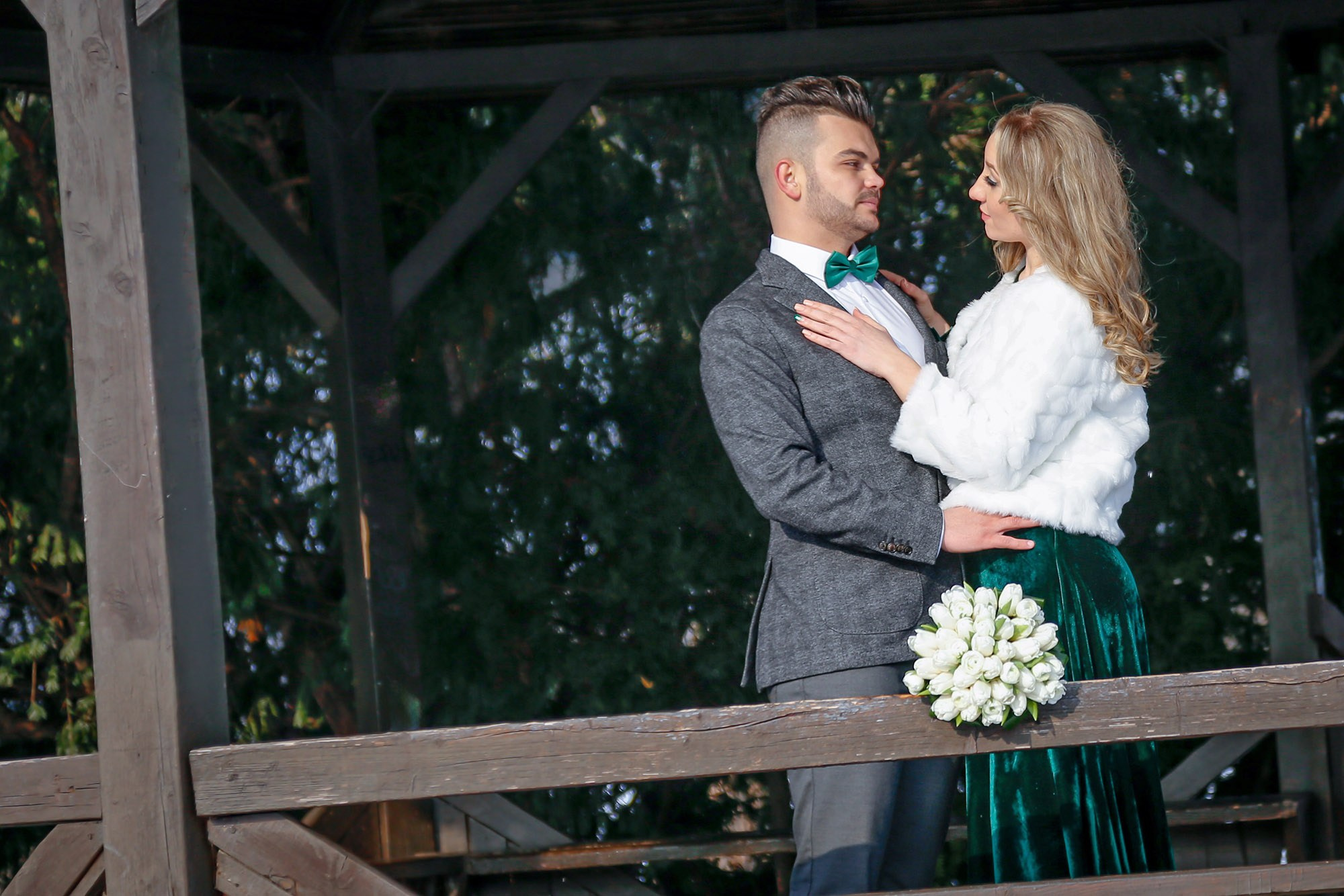 The bride and groom embracing tightly inside the wooden gazebo, a warm and affectionate moment captured during the cold season.