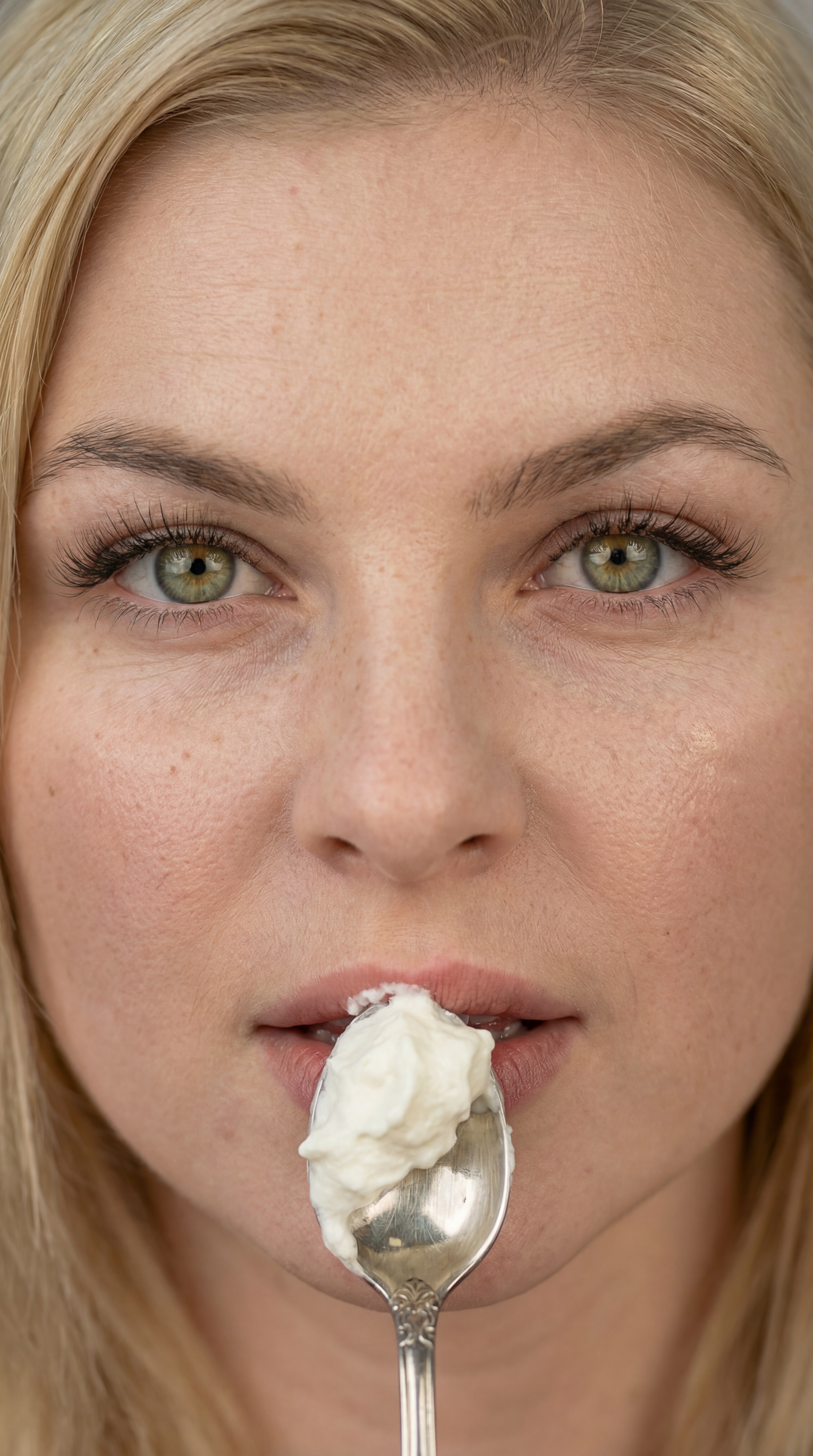 Extreme close-up portrait of blonde woman with spoon of whipped cream near lips, natural skin texture beauty photography, soft diffused light, minimal composition, high detail facial portrait