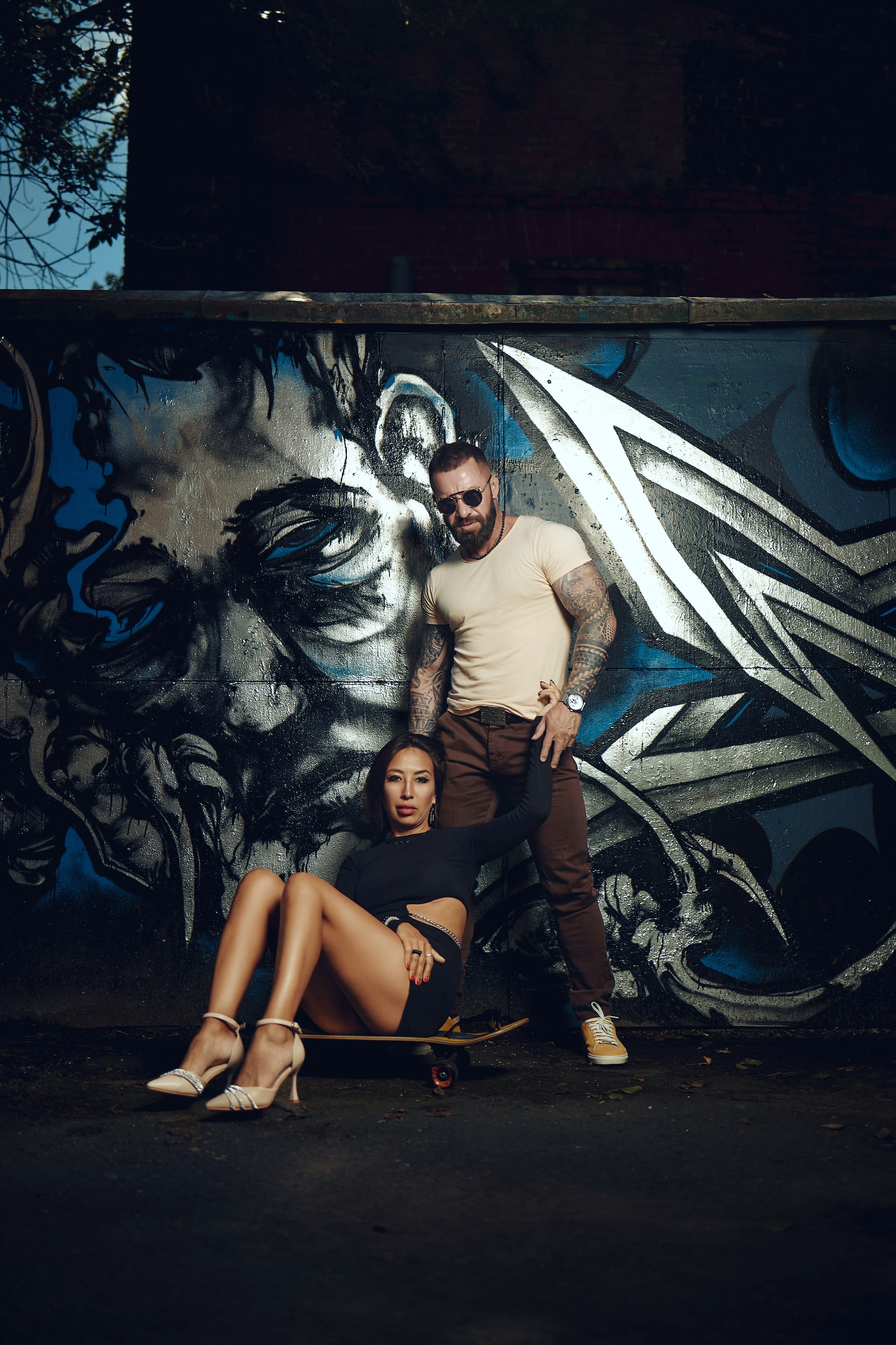 Уличная фотосесия брутальный мужчина и девушка со скейтом у гаражей на фоне граффити
