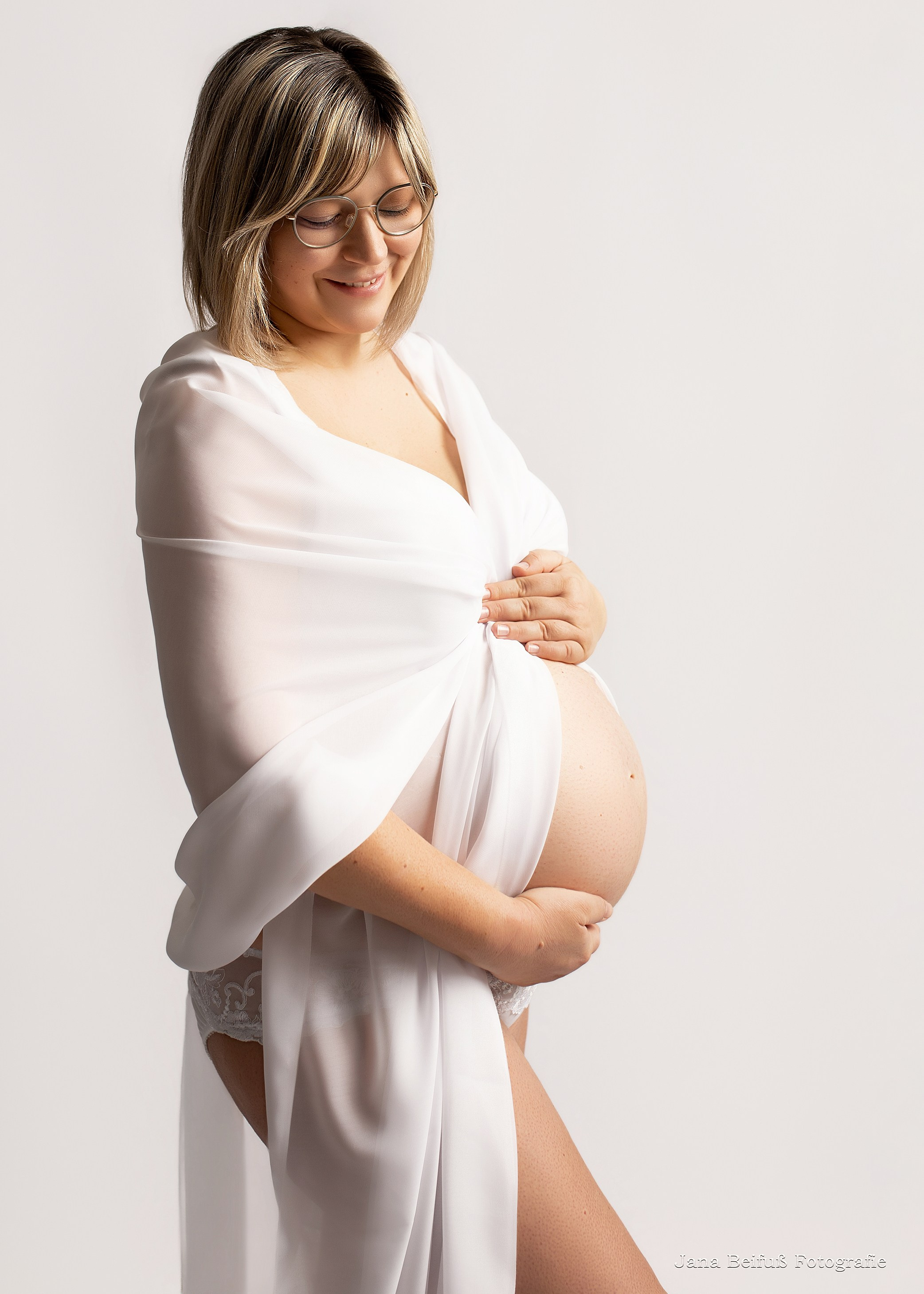 Werdende Mama in weißem Tüll lächelt und hält Babybauch mit den Händen bei Jana Beifuß Fotografie in Weißenhorn bei Ulm und Umgebung Memmingen Krumbach Illertissen Senden