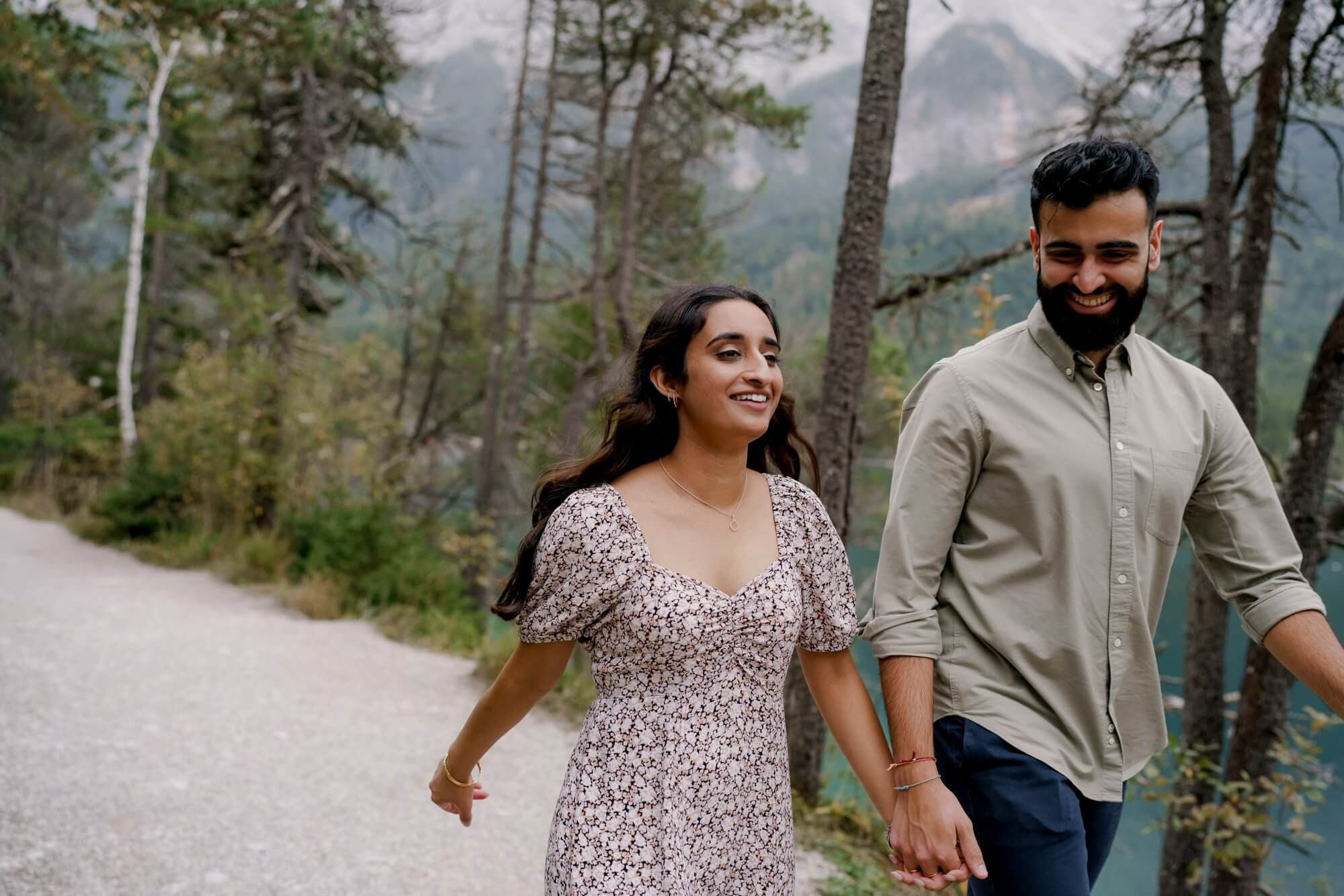 Couple walking hand-in-hand toward camera on forest path at Eibsee during engagement session in Germany
