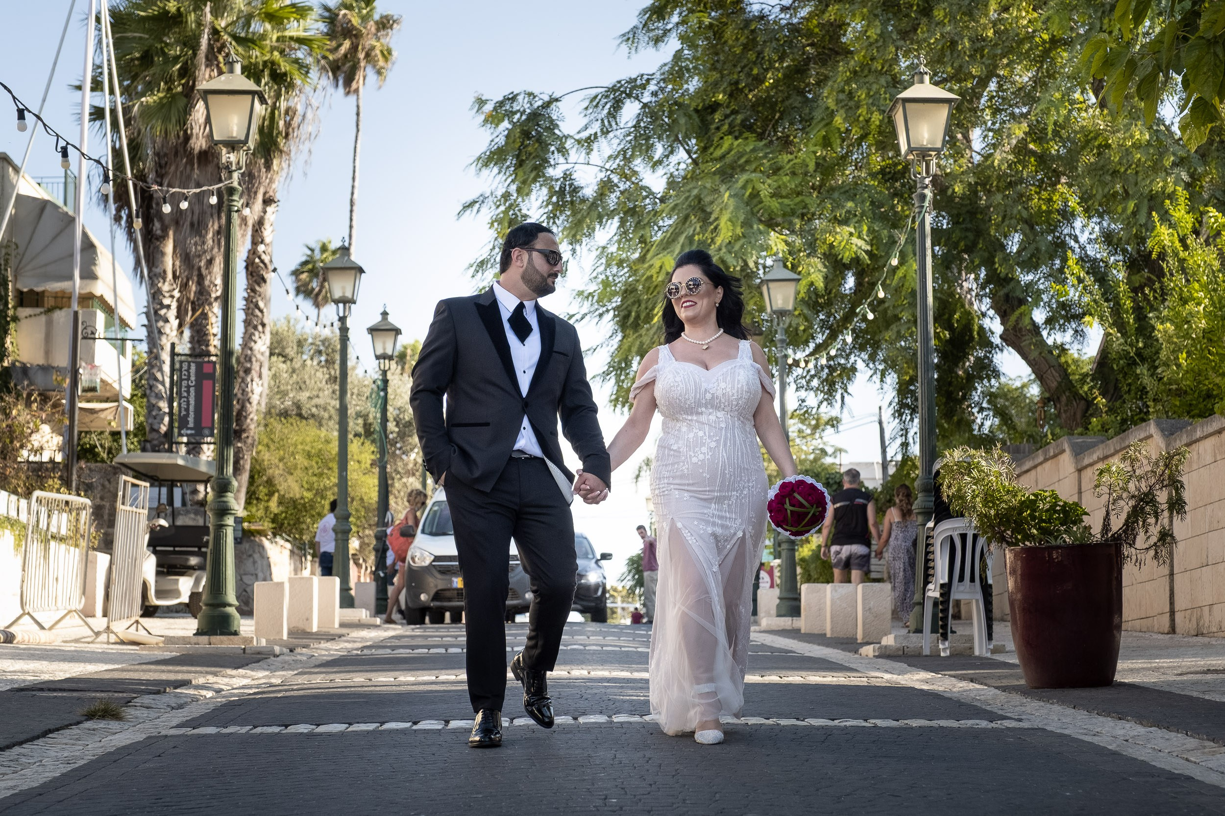 Sara and Emil wear sunglasses as they walk hand in hand along the street