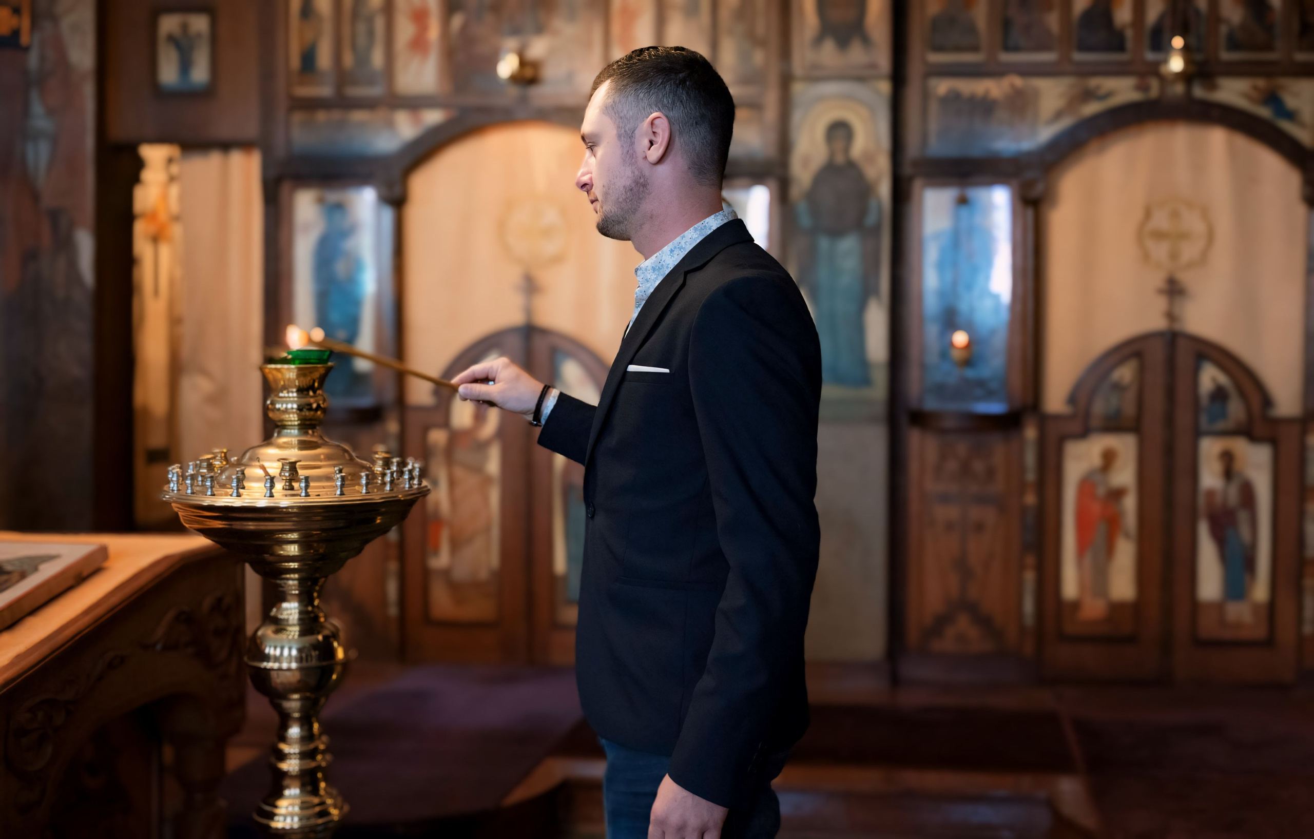 A young man in a black suit lights a candle in a church