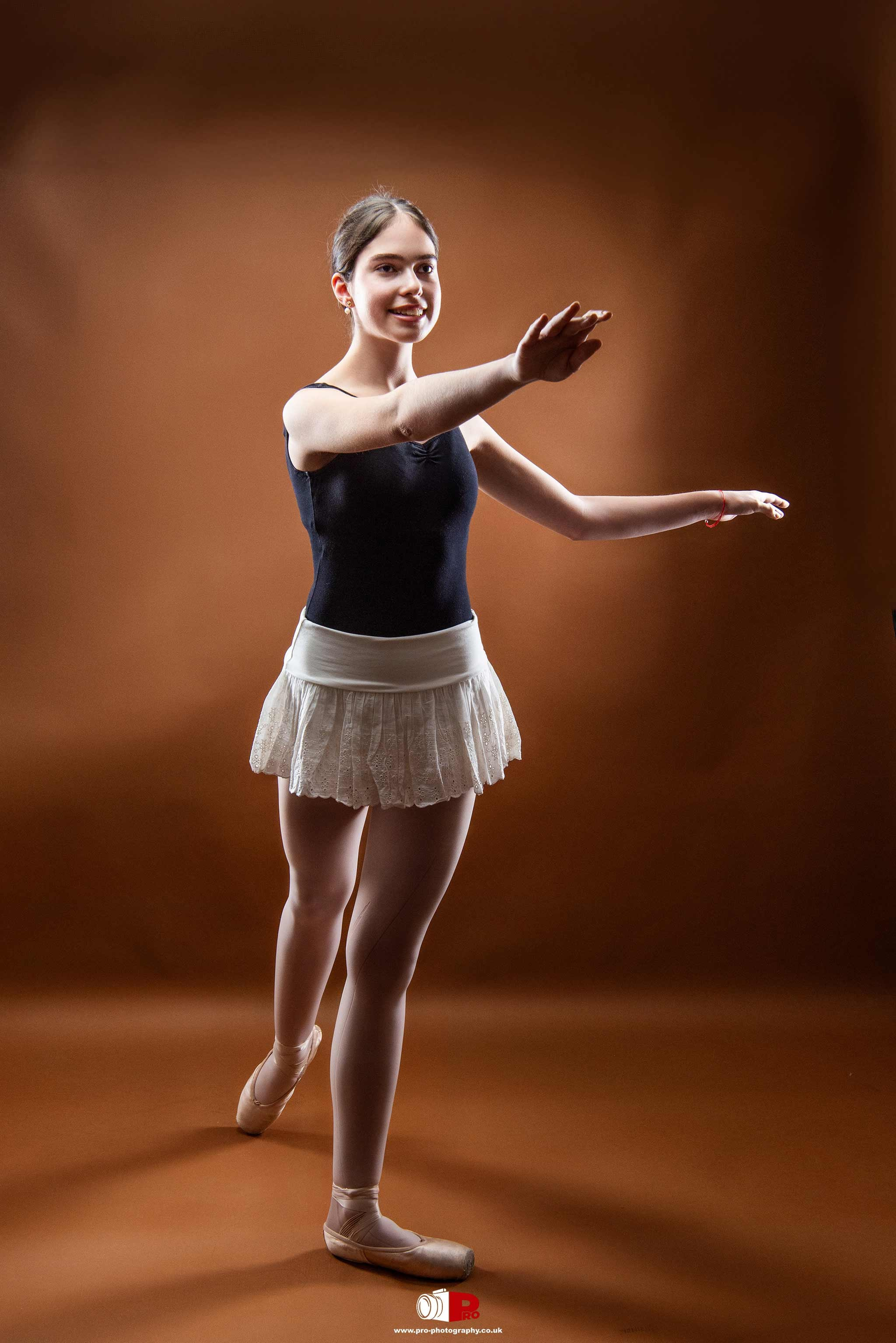 A young ballet dancer in a delicate white skirt and black leotard performing a graceful pose in a studio setting.